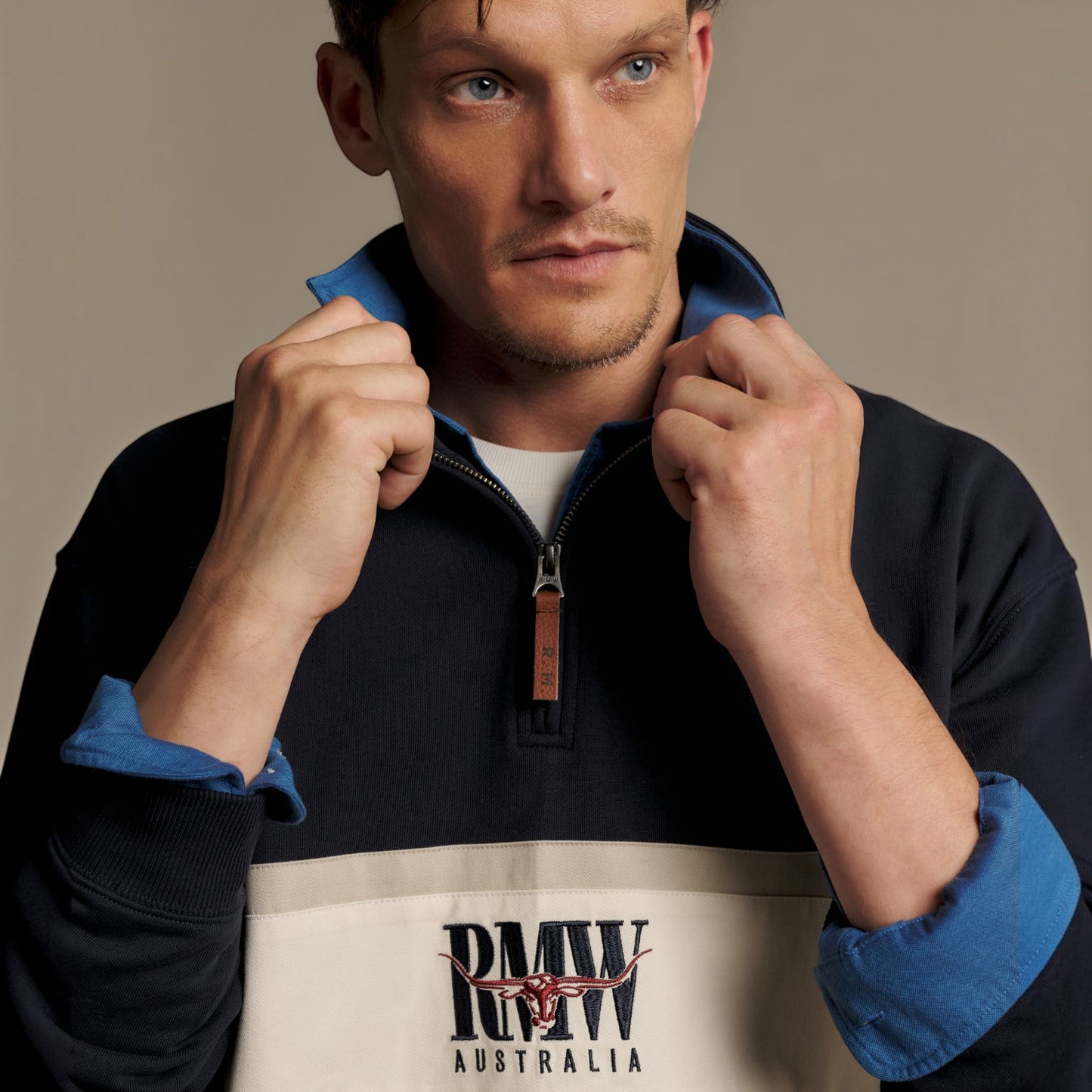 A man wearing a color-blocked quarter-zip sweatshirt with navy, blue, and cream panels, featuring a 'RMW Australia' logo on the front.