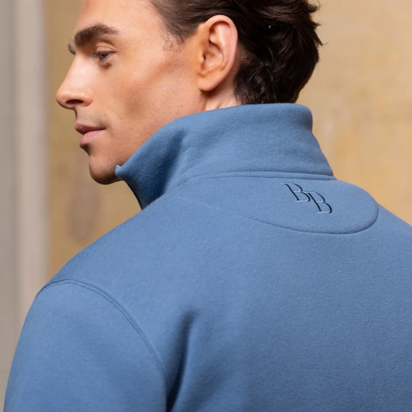 Man wearing a blue jacket with a logo on the back, against a neutral background
