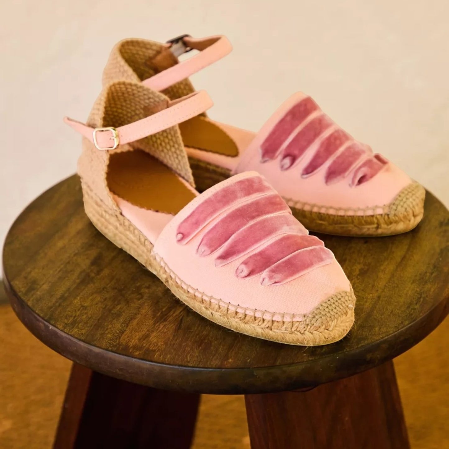 Pink espadrille sandals with jute sole on a wooden stool against a beige background