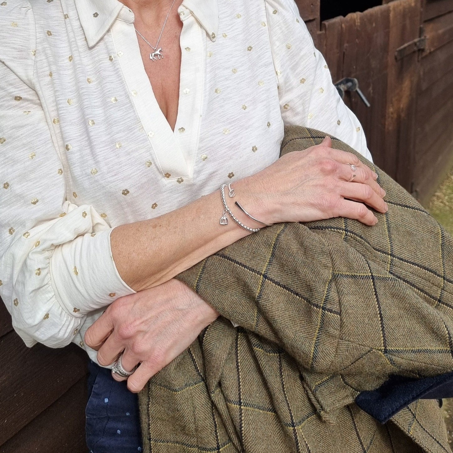 Person wearing a white blouse with gold polka dots and a green jacket, sitting against a wooden wall.