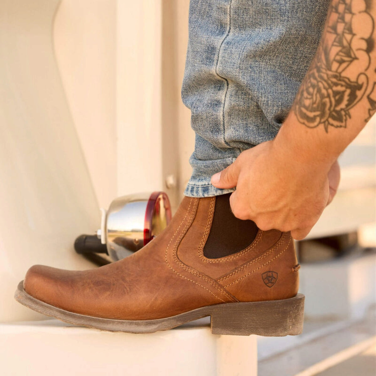Person wearing a brown leather boot with a visible brand logo, standing on a boat.