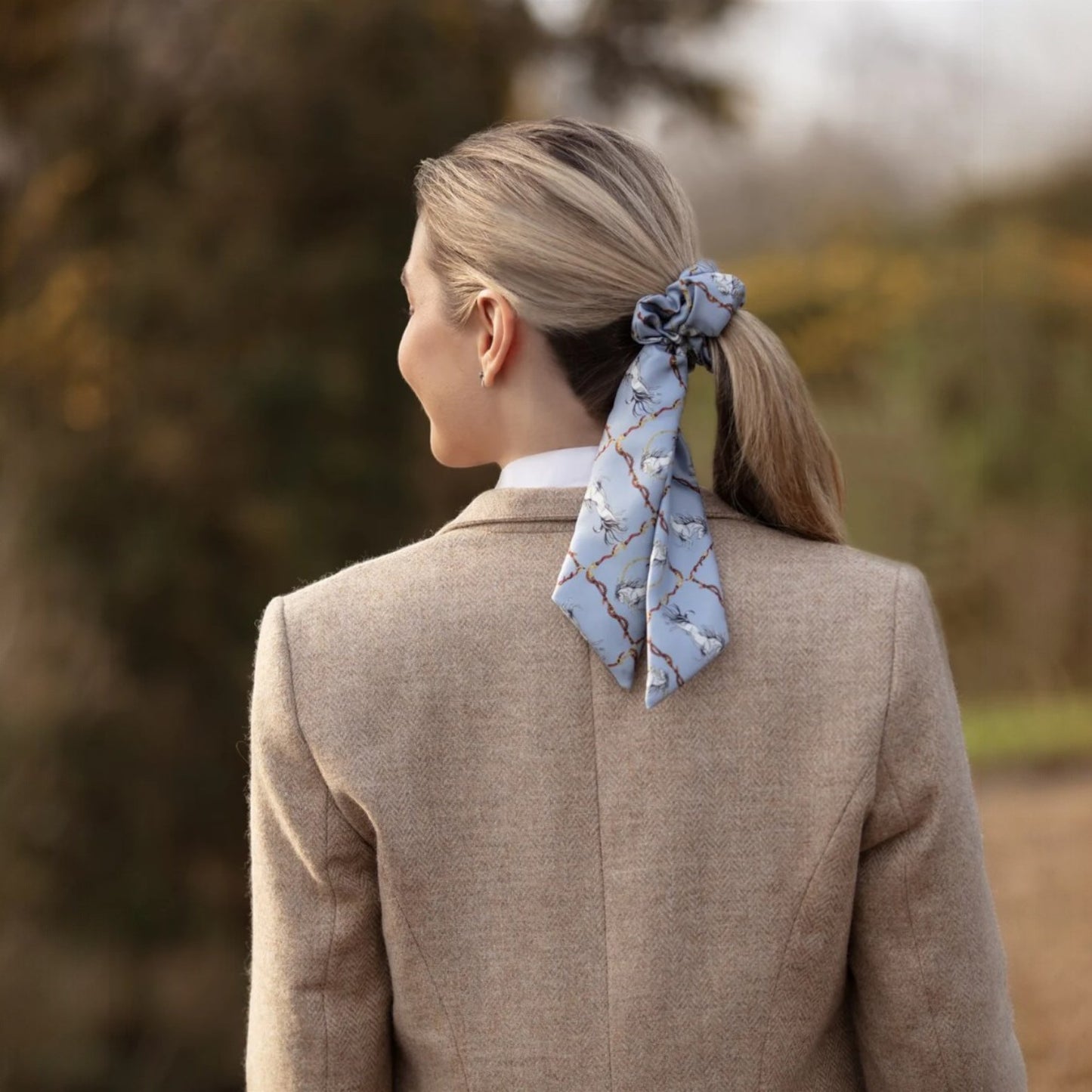 Person wearing a light brown coat with a blue patterned scarf tied around their neck, standing outdoors.