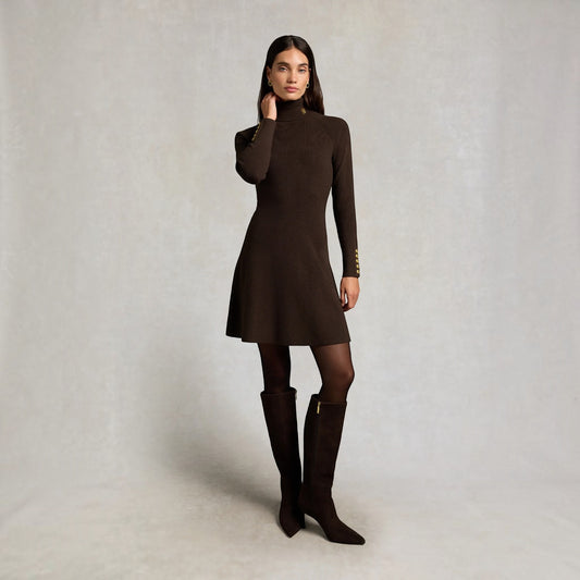 A woman modeling a dark brown mock-neck long-sleeve dress with gold button accents on the cuffs, paired with dark brown tights and matching knee-high boots, against a neutral light gray studio background.