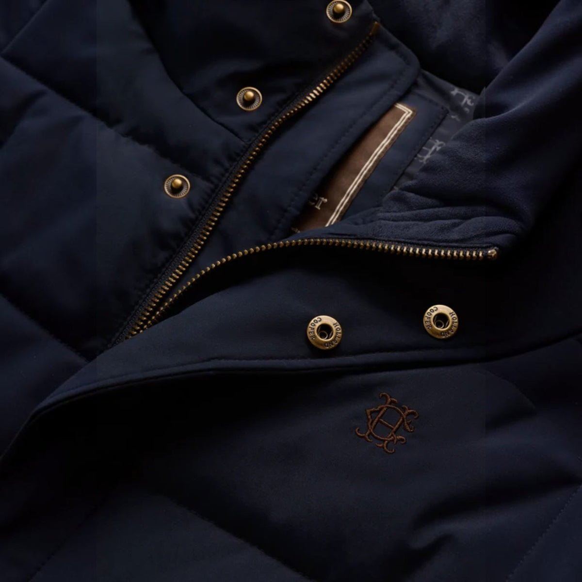 Close-up of a dark navy puffer jacket showing the chest area with gold-tone snap buttons, a zipper, and a small embroidered logo.