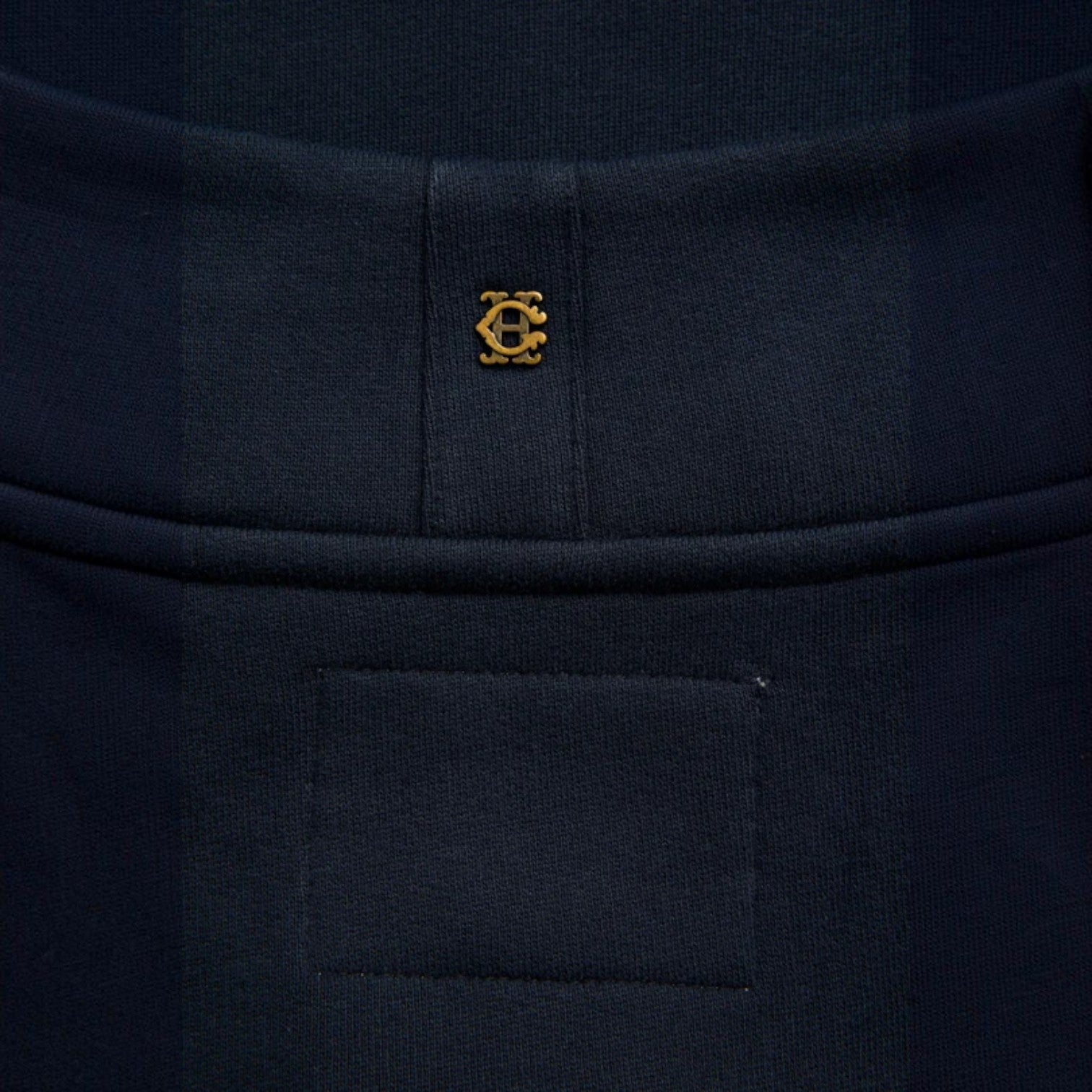 Close-up of a dark navy knit garment with a small gold embroidered circular logo centered below a waistband seam.