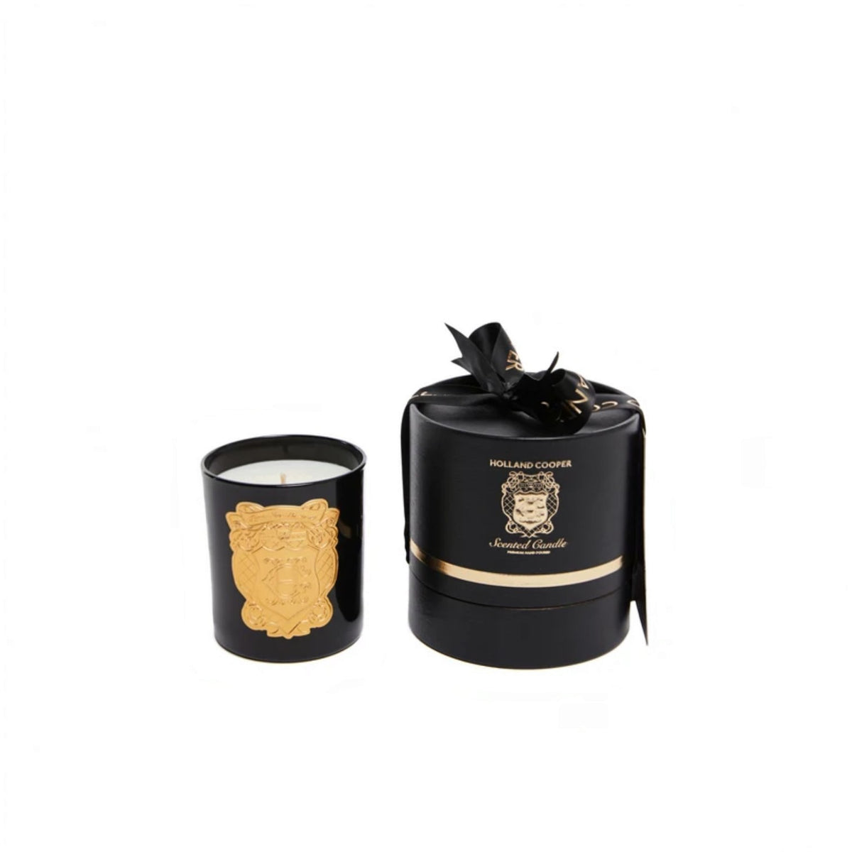 A black glass jar candle with a gold crest design next to its matching black cylindrical box with a black ribbon bow. The box features gold lettering that reads 'HOLLAND Cooper' and 'Extrait de Parfum'.