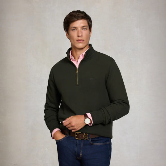 Man wearing a black quarter-zip sweater over a pink shirt with a neutral background