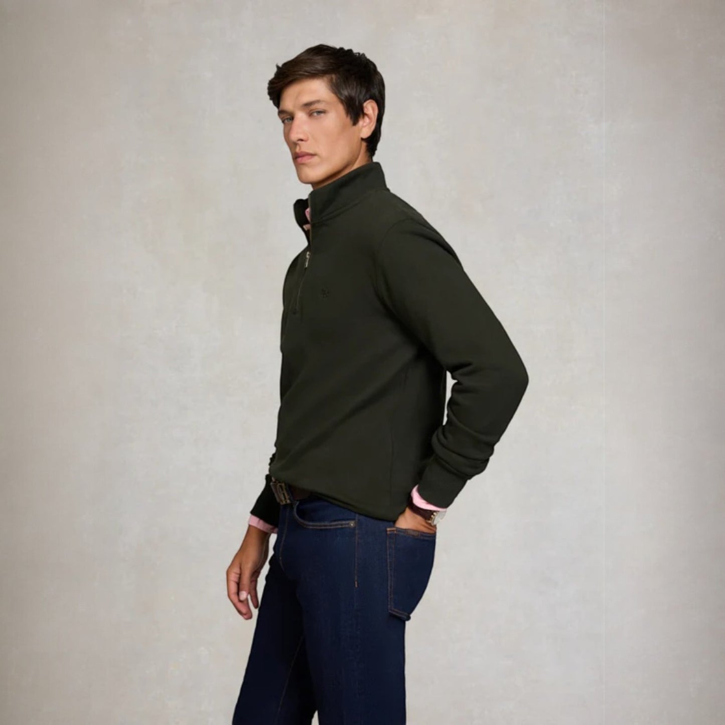 Man wearing a dark green half-zip sweater and blue jeans against a plain background