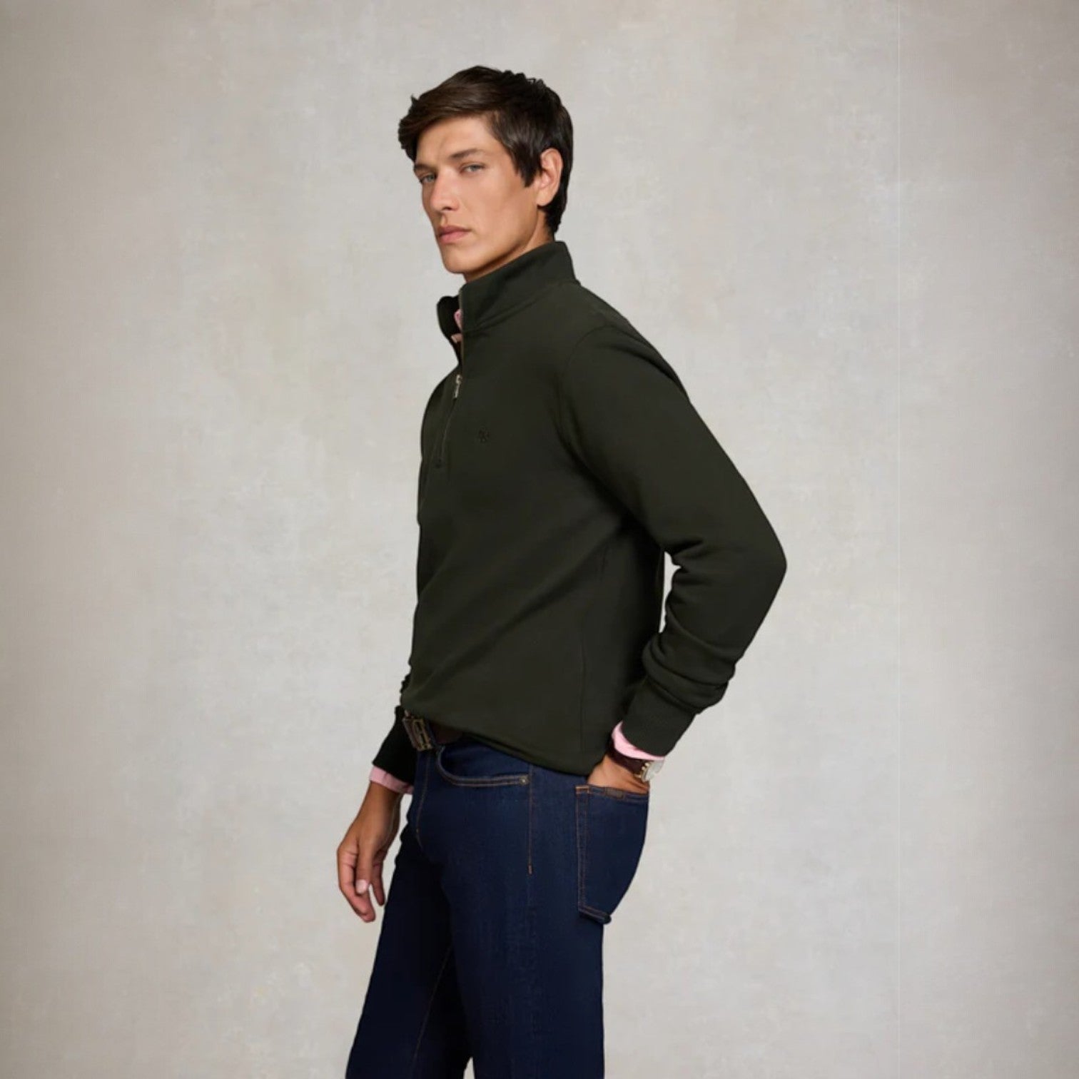 Man wearing a dark green half-zip sweater and blue jeans against a plain background