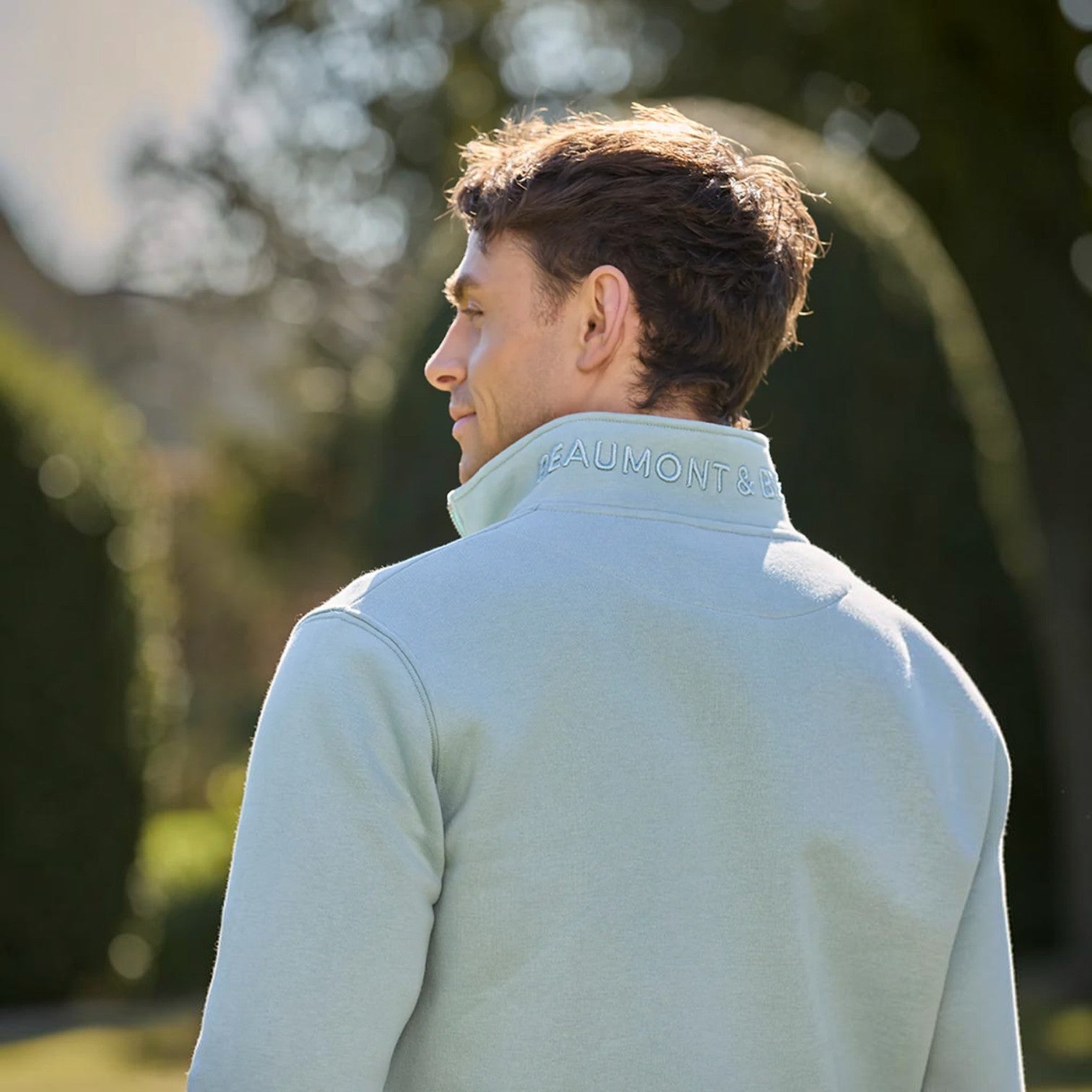Man wearing a light blue sweatshirt with 'Beaumont' branding, standing outdoors.