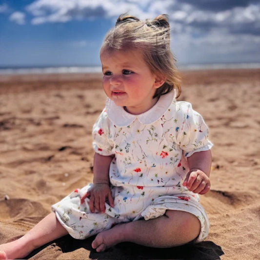 Child in a floral dress sitting on a sandy beach with ocean and sky in the background
