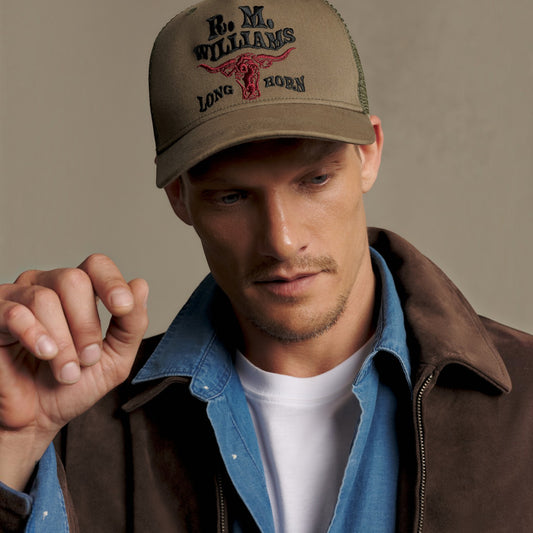 A man wearing a tan trucker hat with 'R.M.