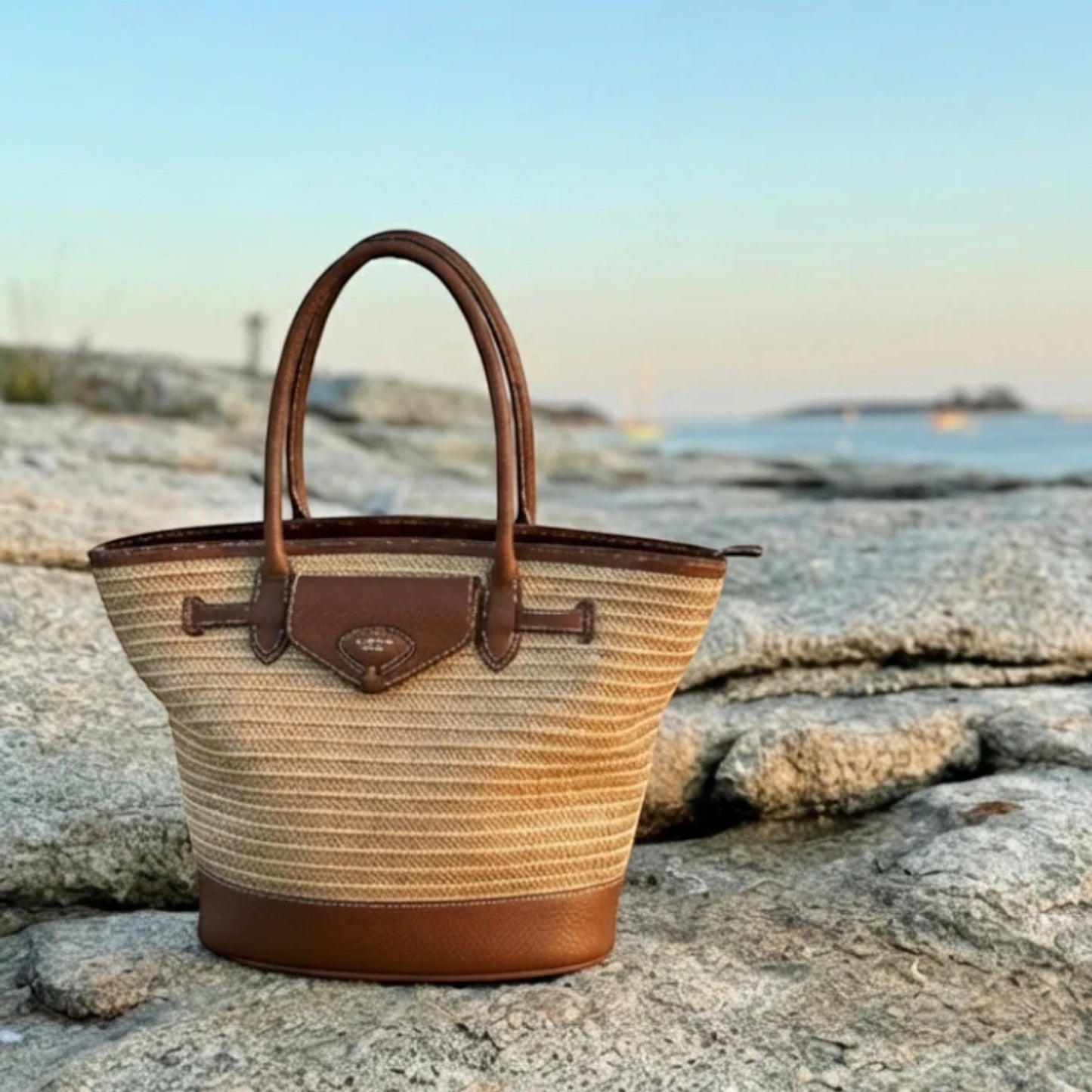 Woven handbag with brown leather accents on a rocky surface with a blurred natural background