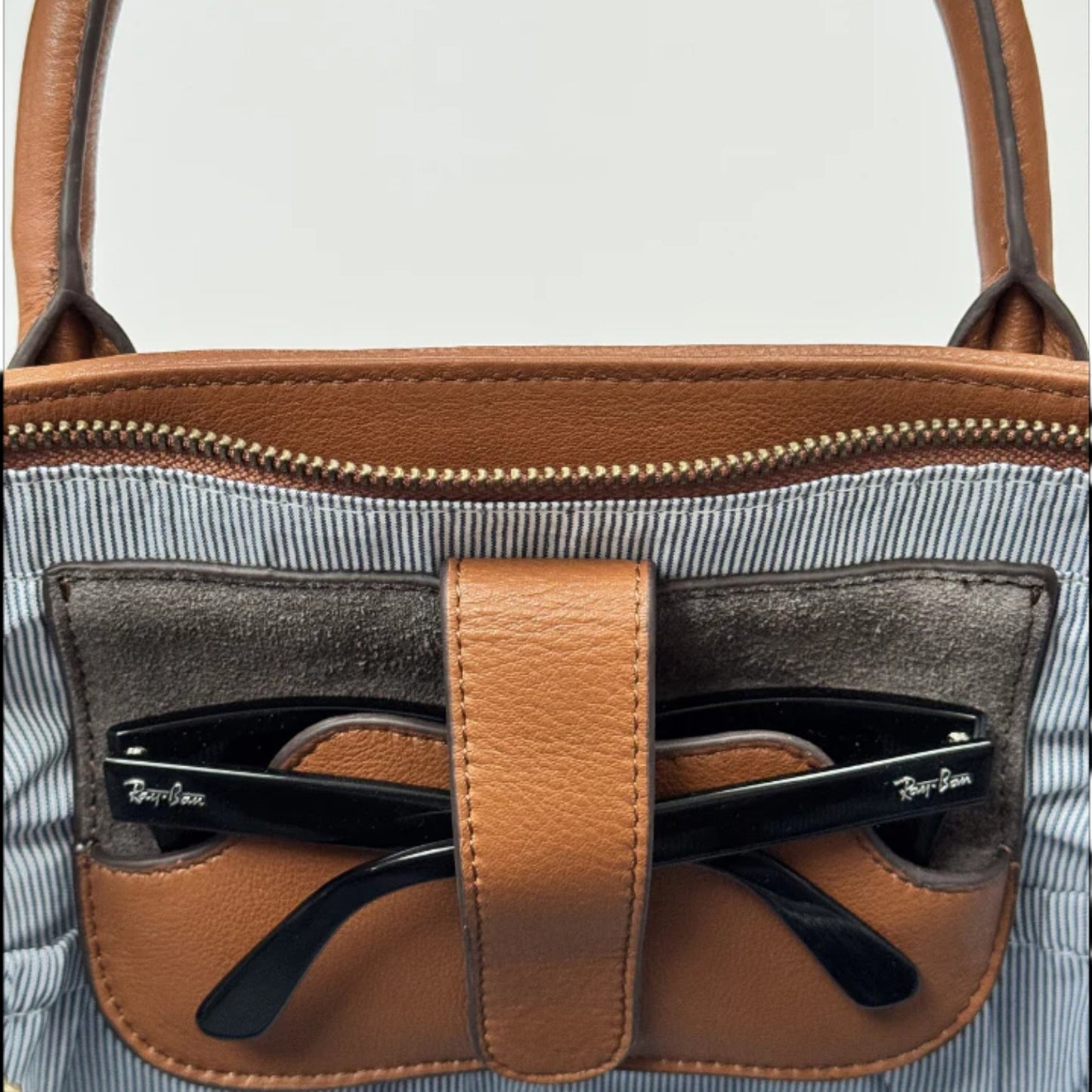 Brown leather handbag with sunglasses pocket on a light gray background