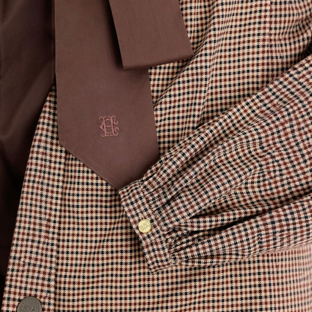 Close-up of a brown and beige gingham patterned jacket with a matching brown tie featuring a tonal embroidered monogram.