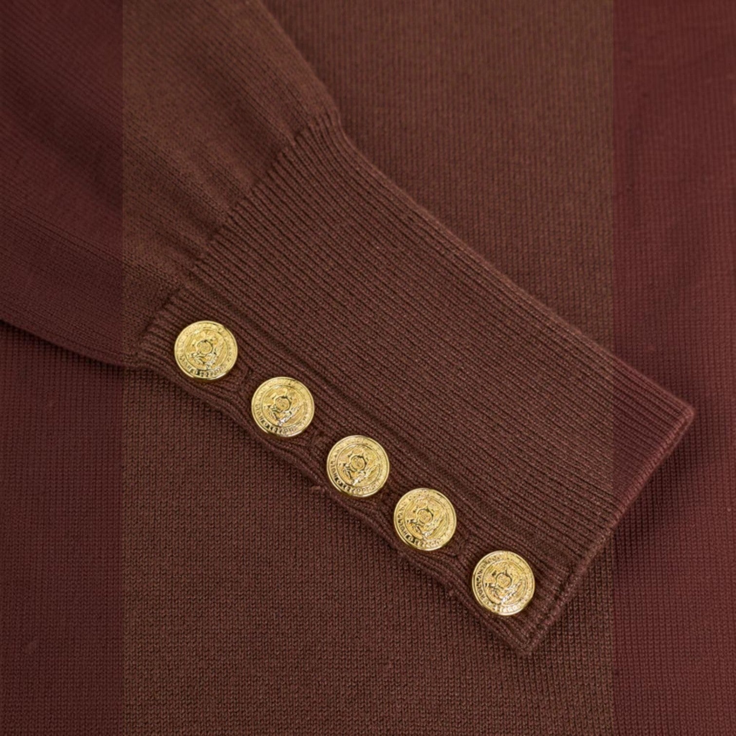 Close-up of a brown ribbed knit garment sleeve with five decorative gold buttons aligned along the cuff.
