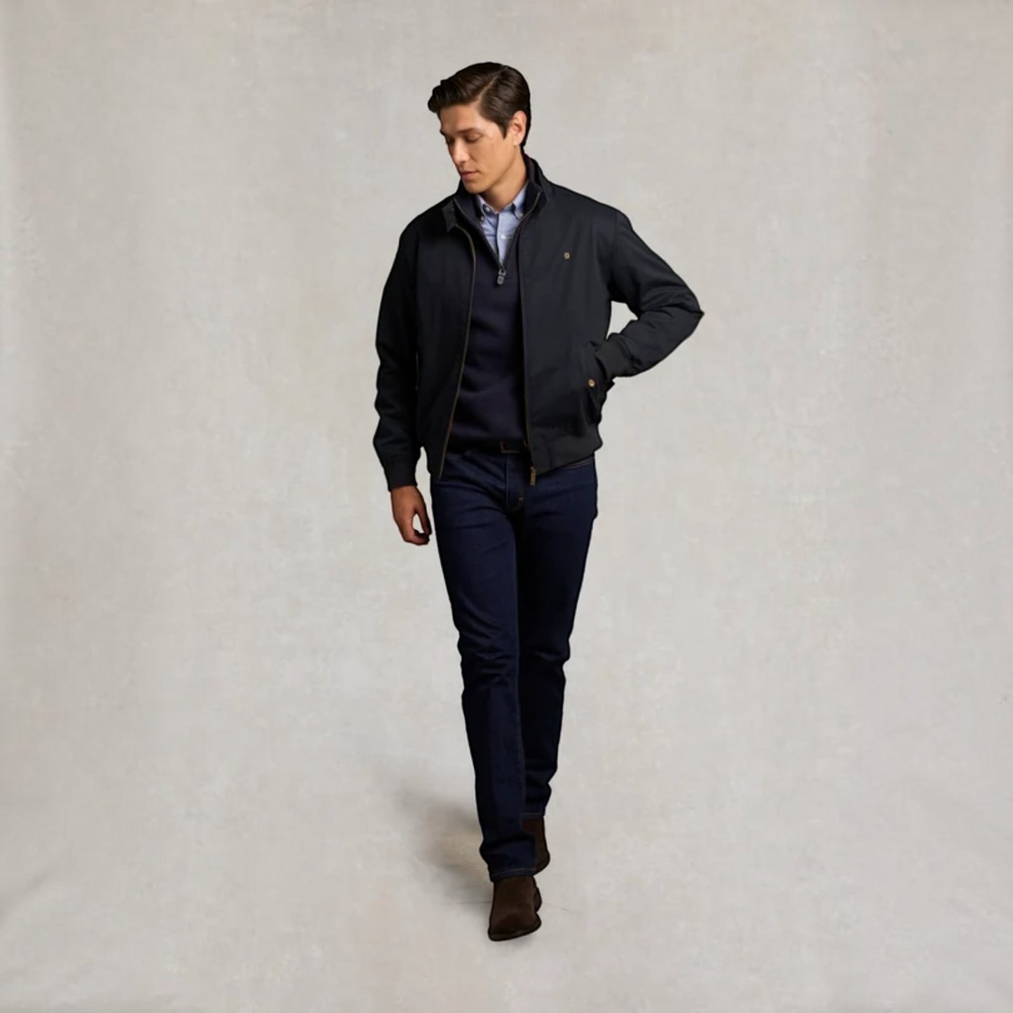 A man modeling a dark navy blue zip-up jacket over a matching navy sweater and trousers, standing against a neutral textured light gray background.