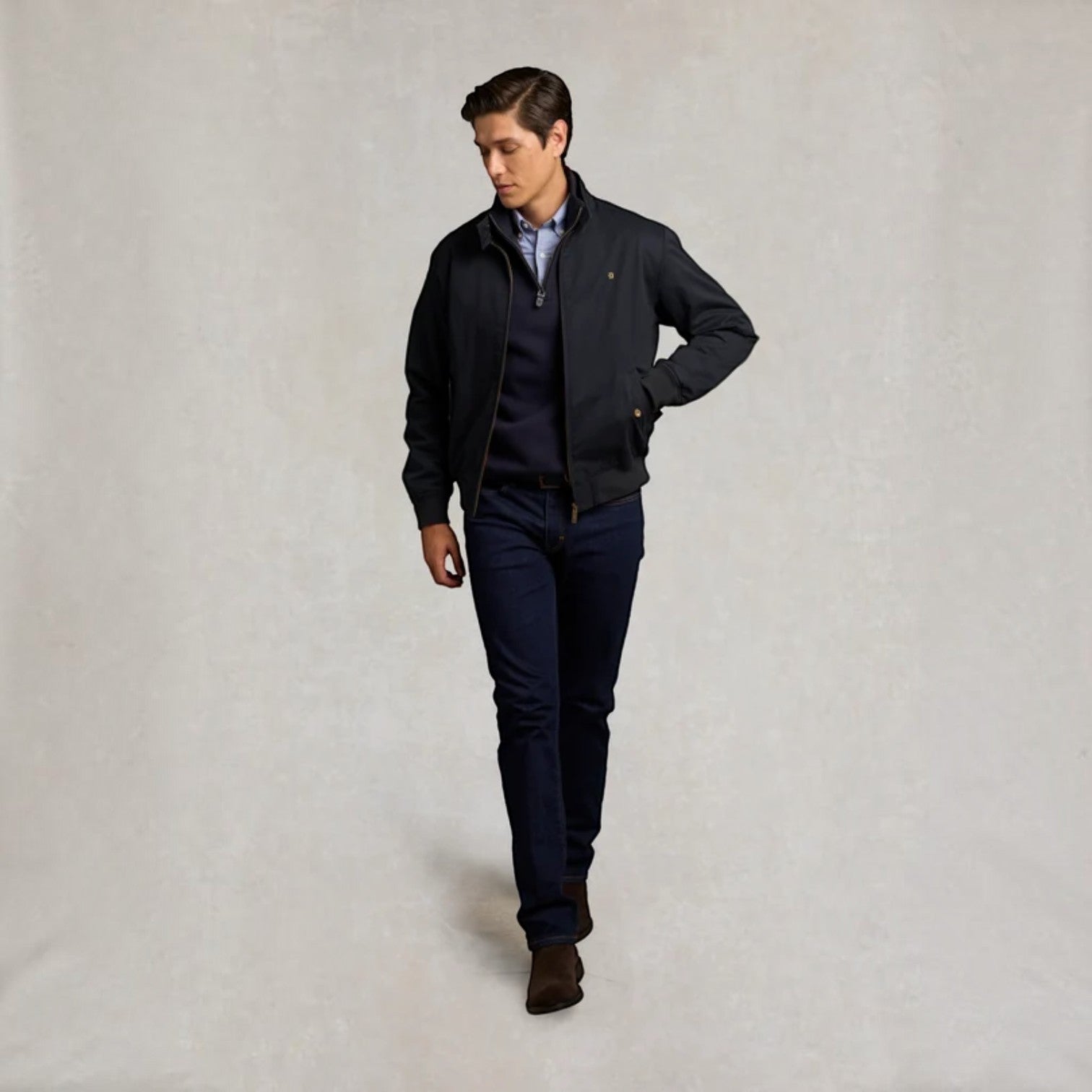 A man modeling a dark navy blue zip-up jacket over a matching navy sweater and trousers, standing against a neutral textured light gray background.