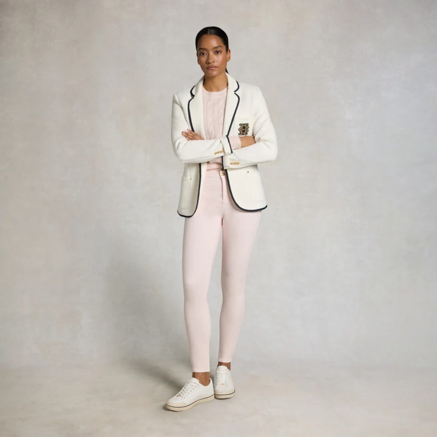Person wearing a white blazer with black accents and pink pants on a plain background