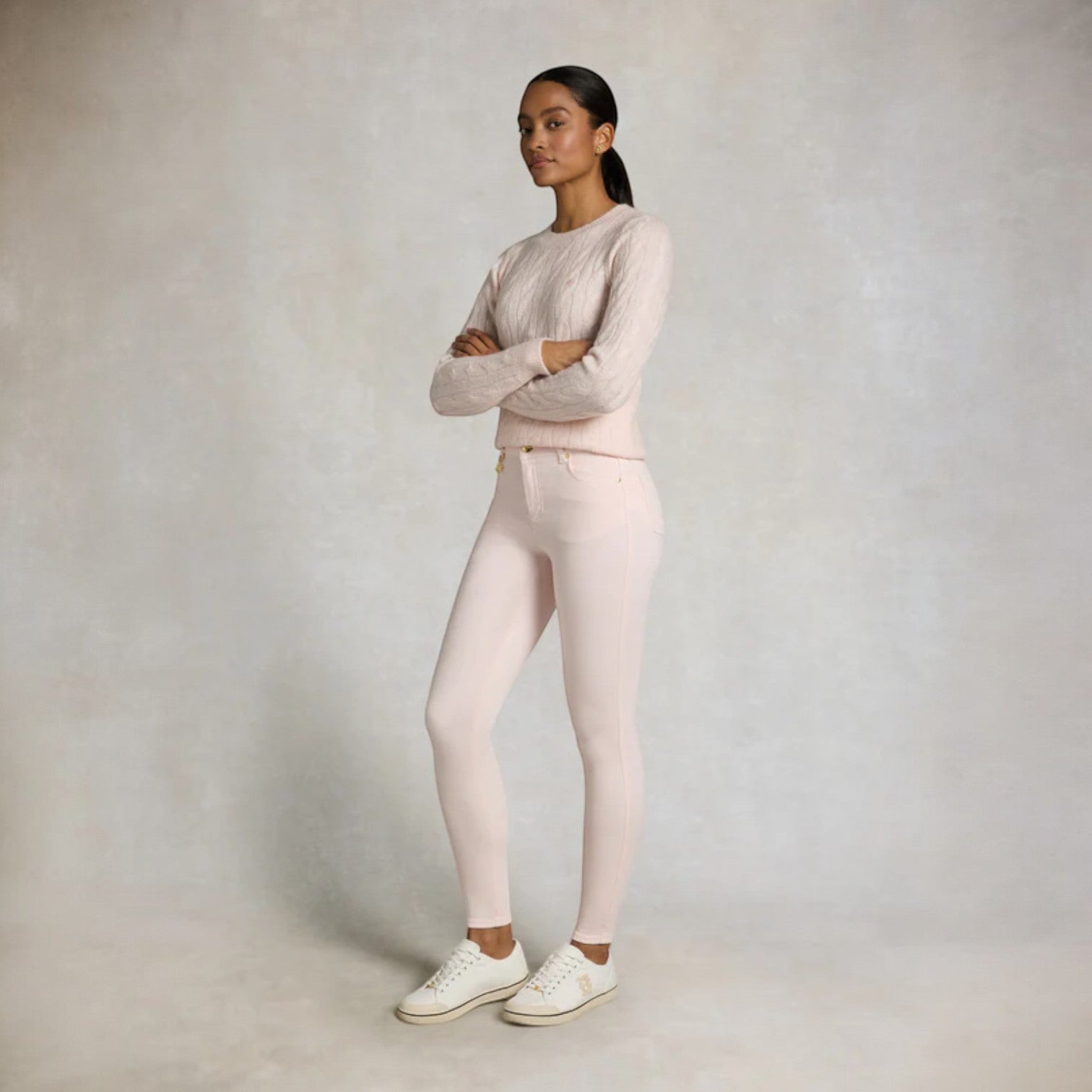 Woman wearing a light pink sweater and pants with white shoes on a plain background
