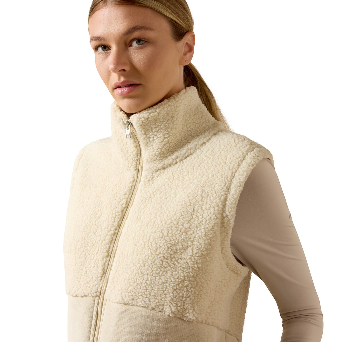 A woman wearing a cream sherpa fleece zip-up vest over a beige long-sleeve top, photographed against a clean white studio background.