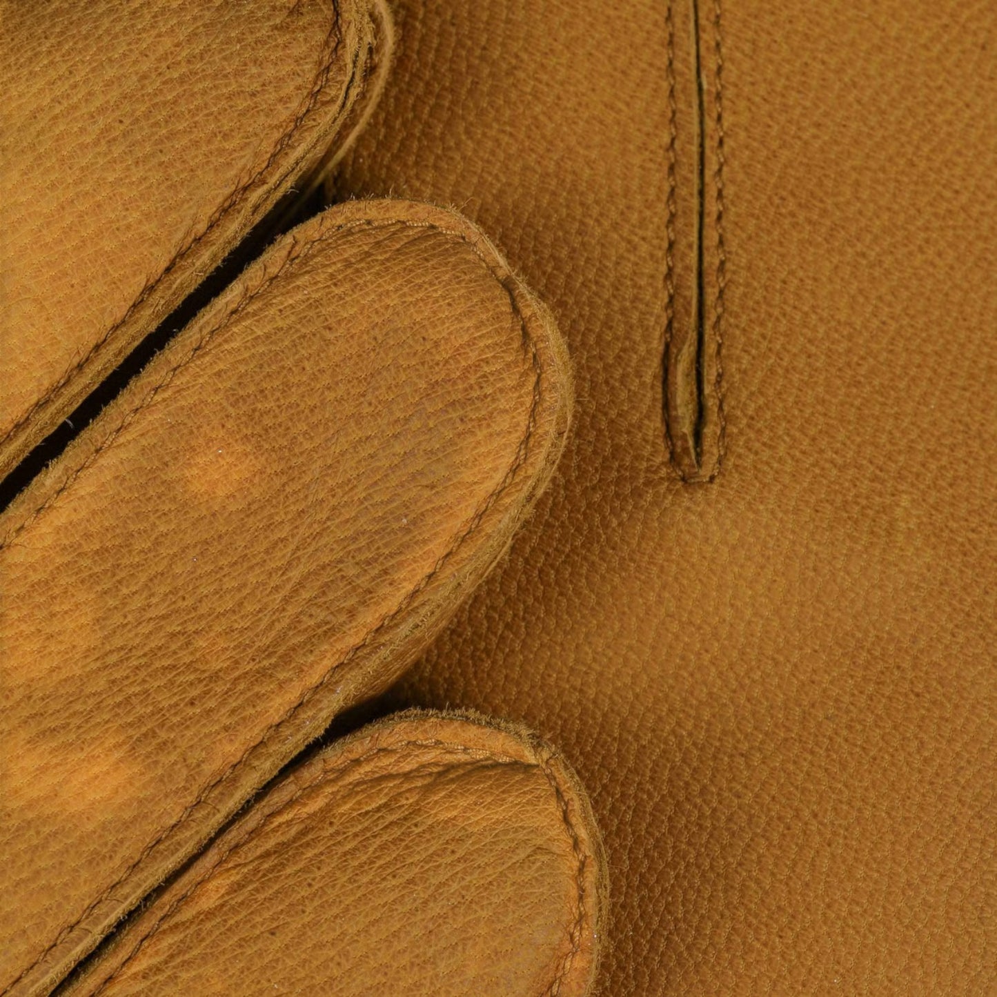 Close-up of a tan leather glove showing the pebbled texture, stitched edges, and a vertical welt pocket.