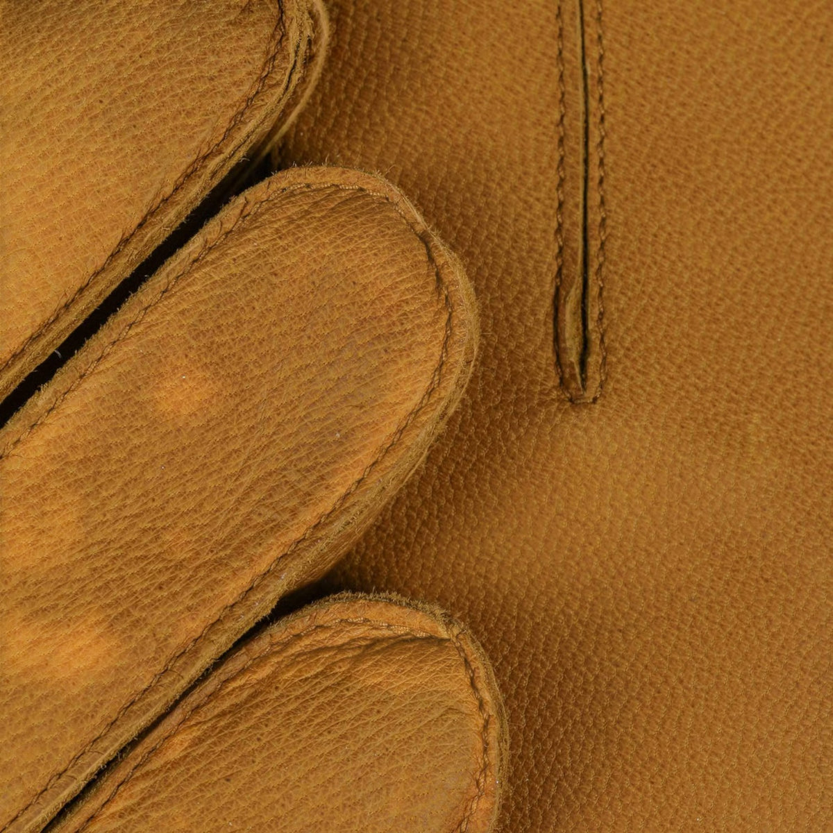 Close-up of a tan leather glove showing the pebbled texture, stitched edges, and a vertical welt pocket.