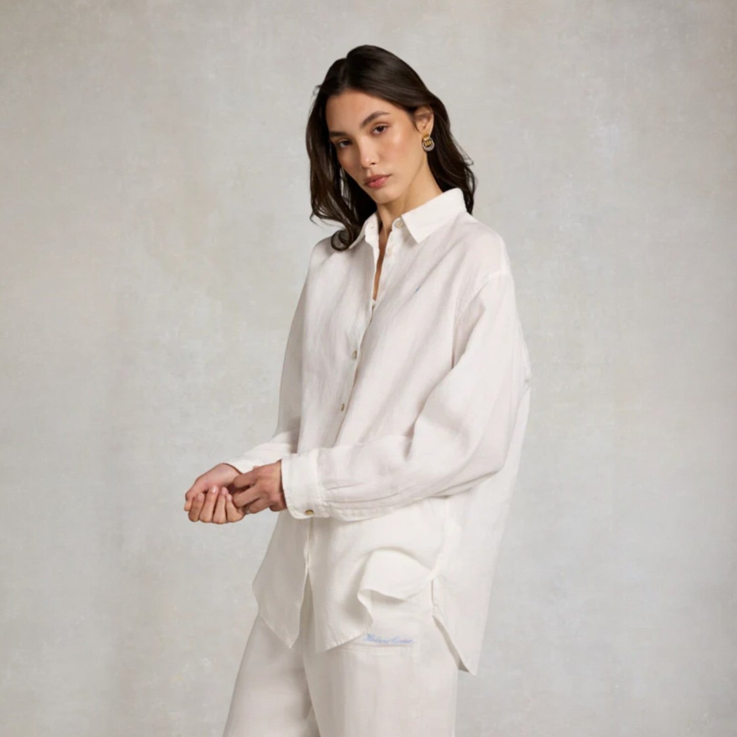 Woman wearing a white shirt and pants against a plain background