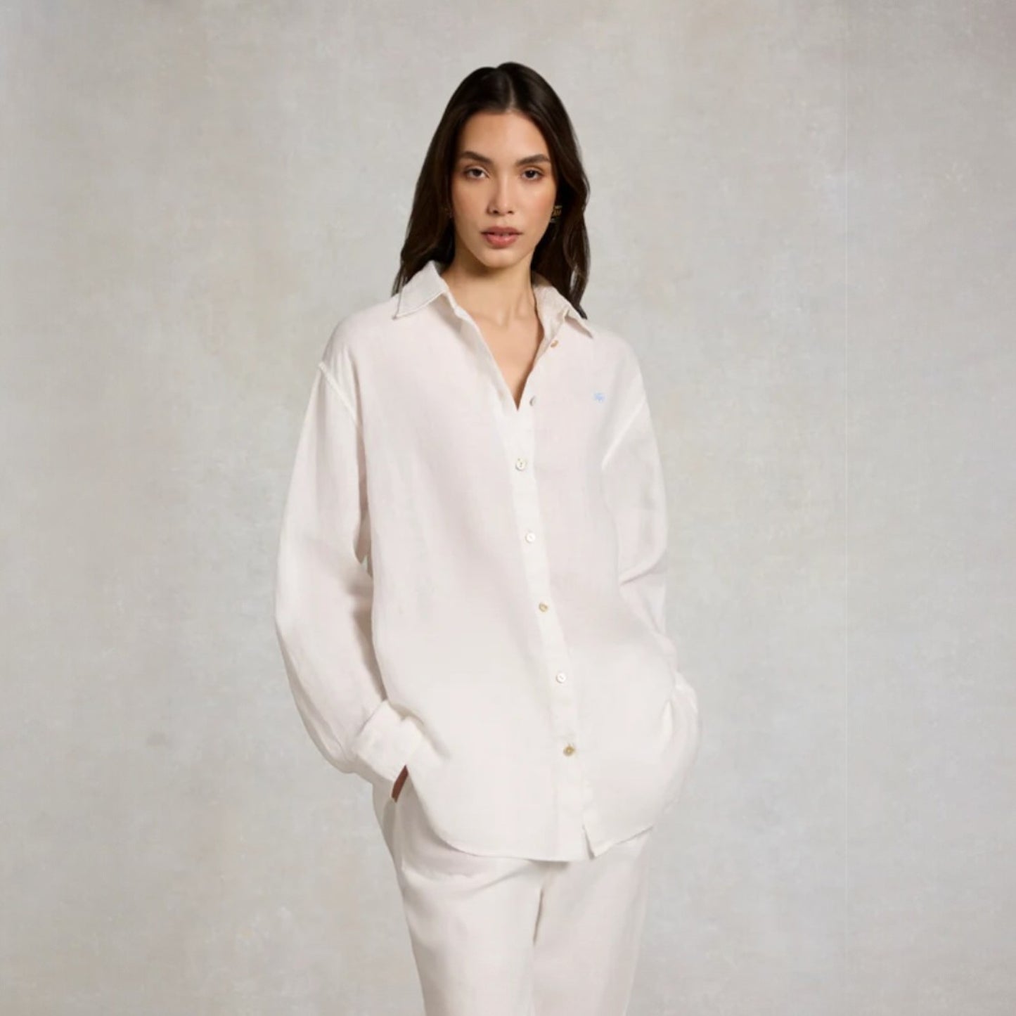 Woman wearing a white shirt and pants against a plain background