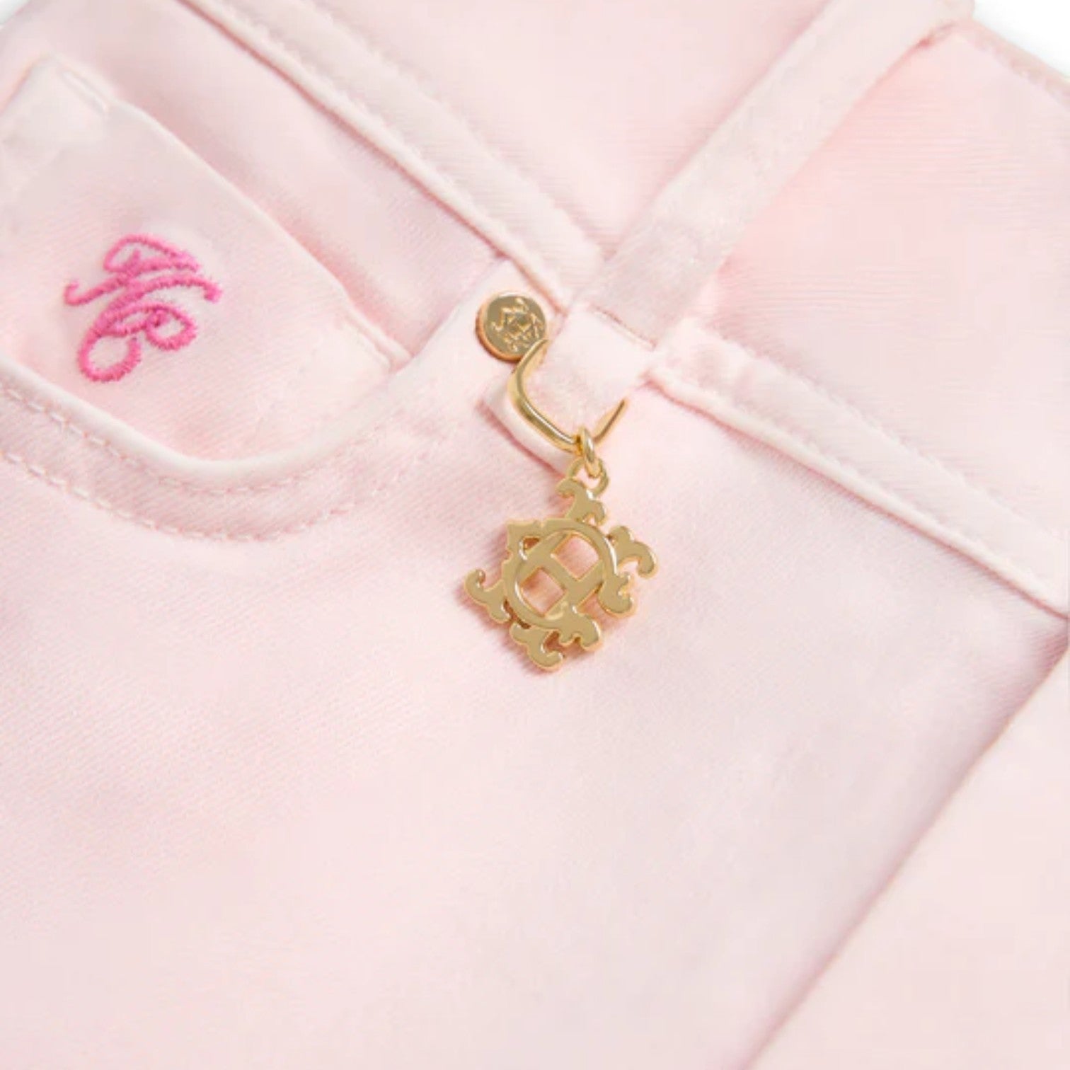 Close-up of a pink garment with a gold brooch and pink lettering on a white background