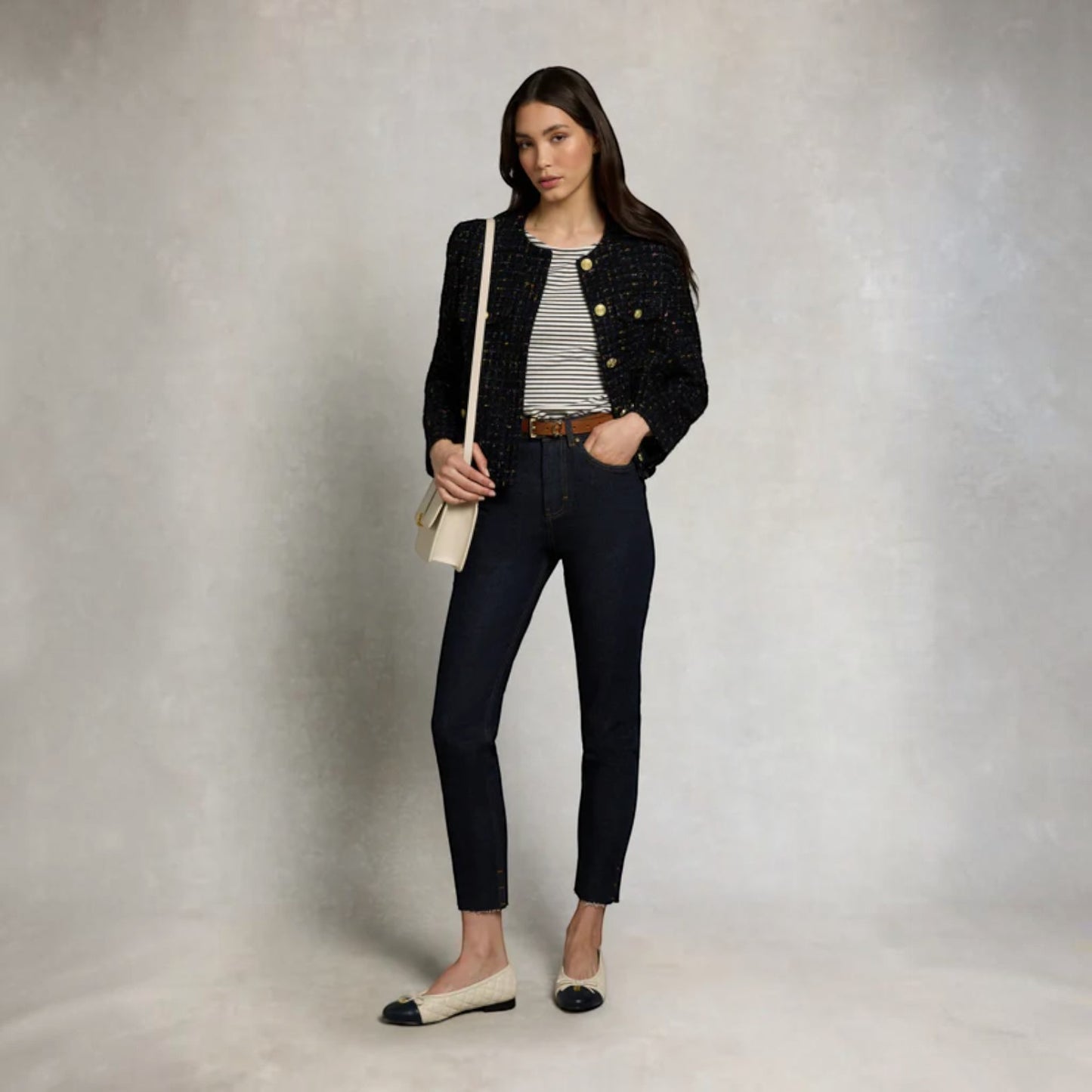 Woman wearing a black jacket, striped shirt, and jeans against a neutral background