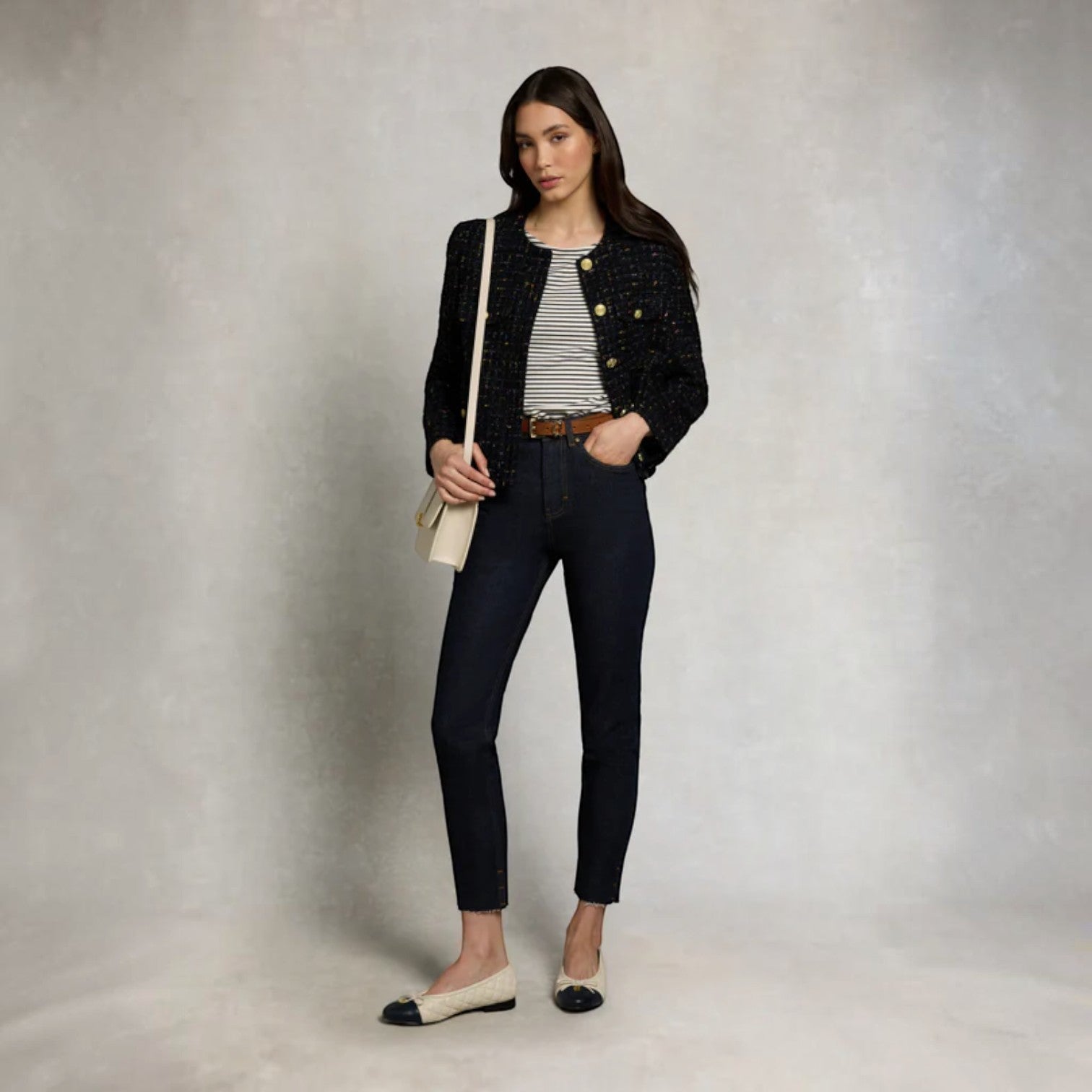 Woman wearing a black jacket, striped shirt, and jeans against a neutral background