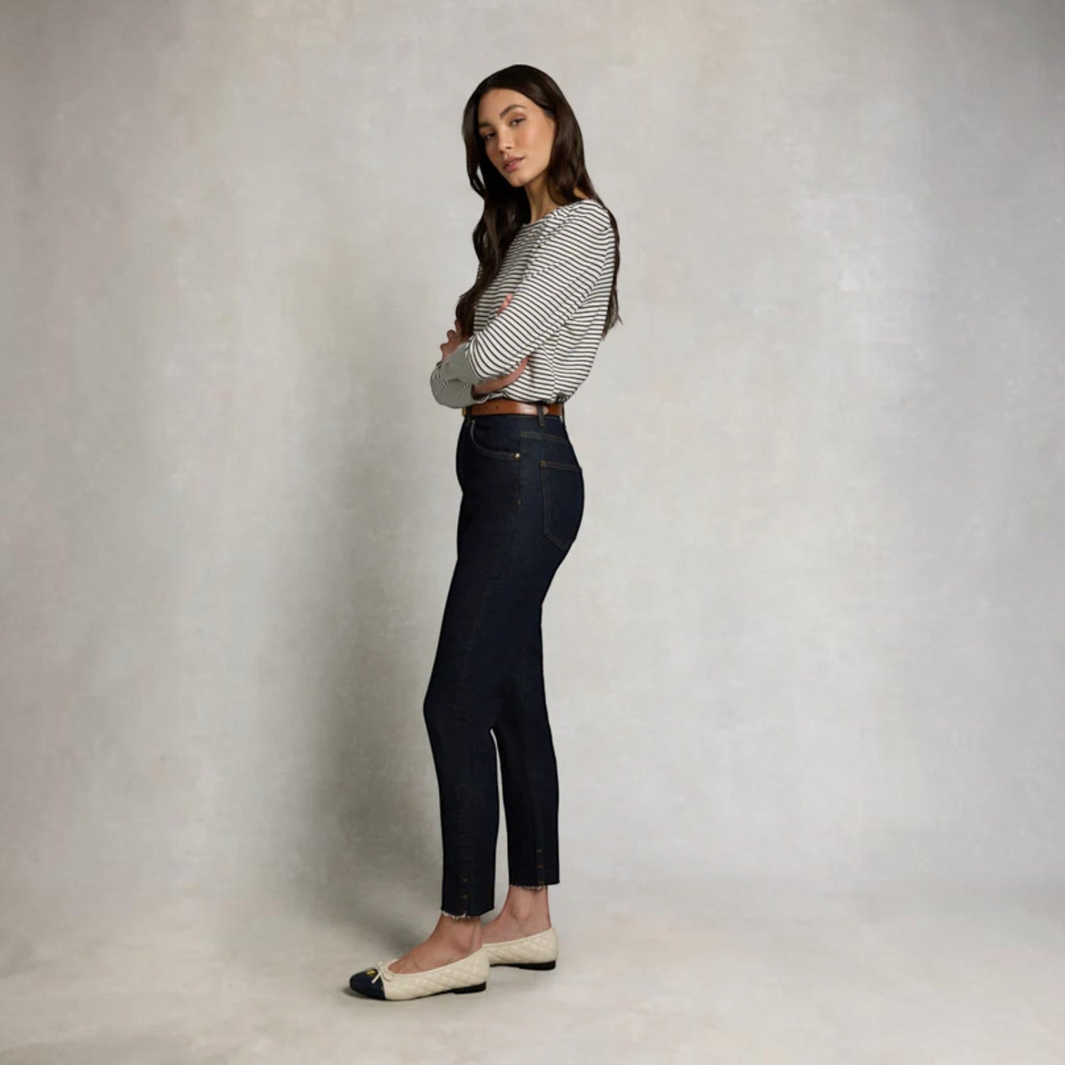 Woman wearing a striped shirt and dark jeans against a plain background
