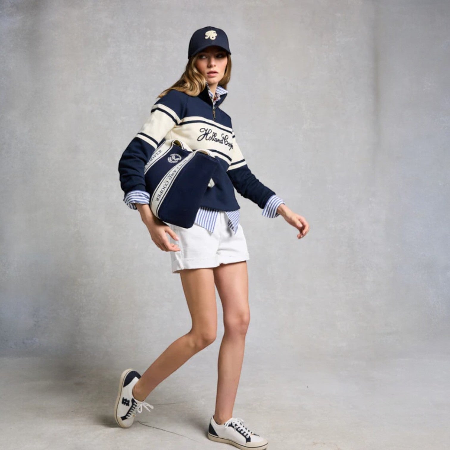 Person wearing a navy and white striped sweater with a cap and shorts on a gray background