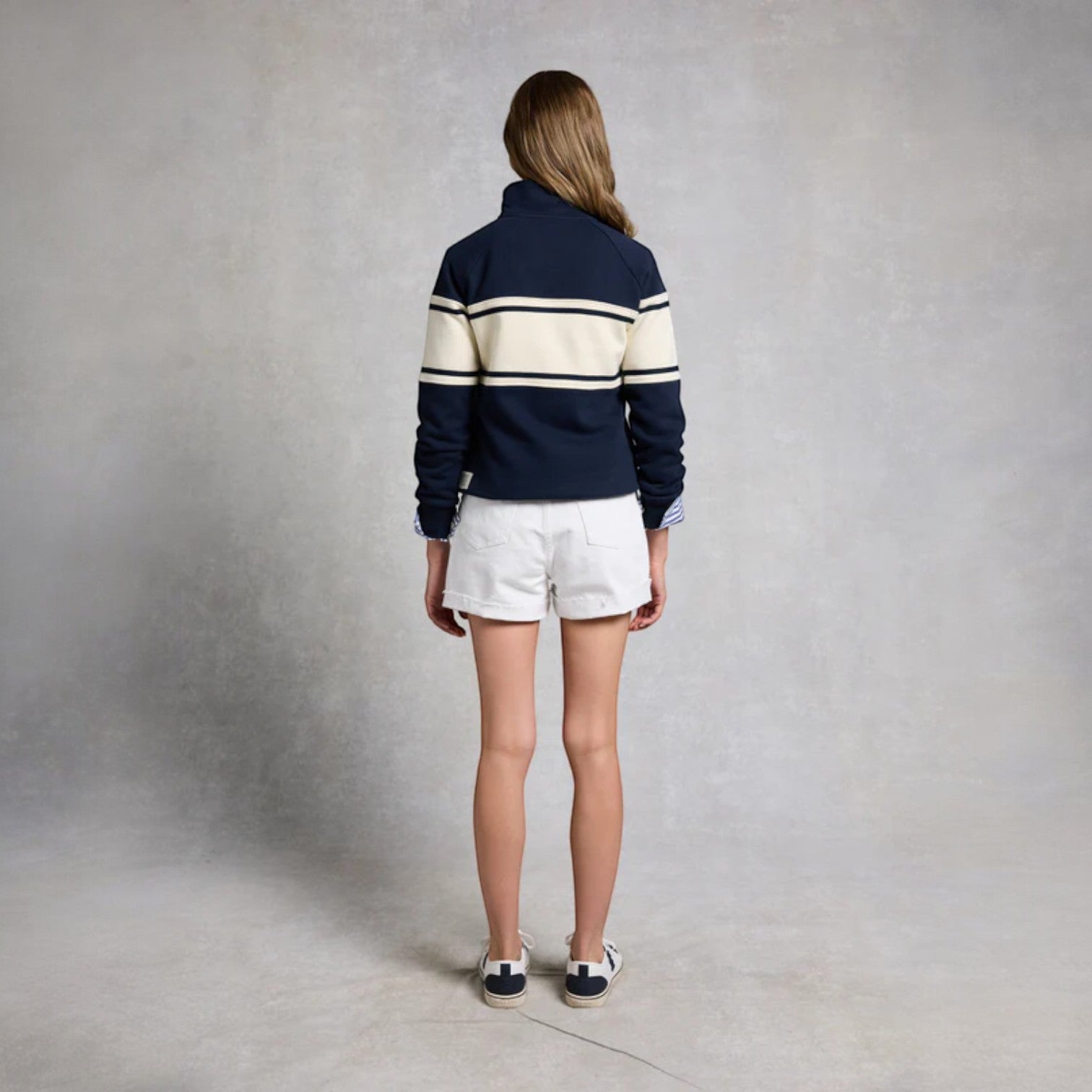 Person wearing a navy and white striped sweater with white shorts on a plain background
