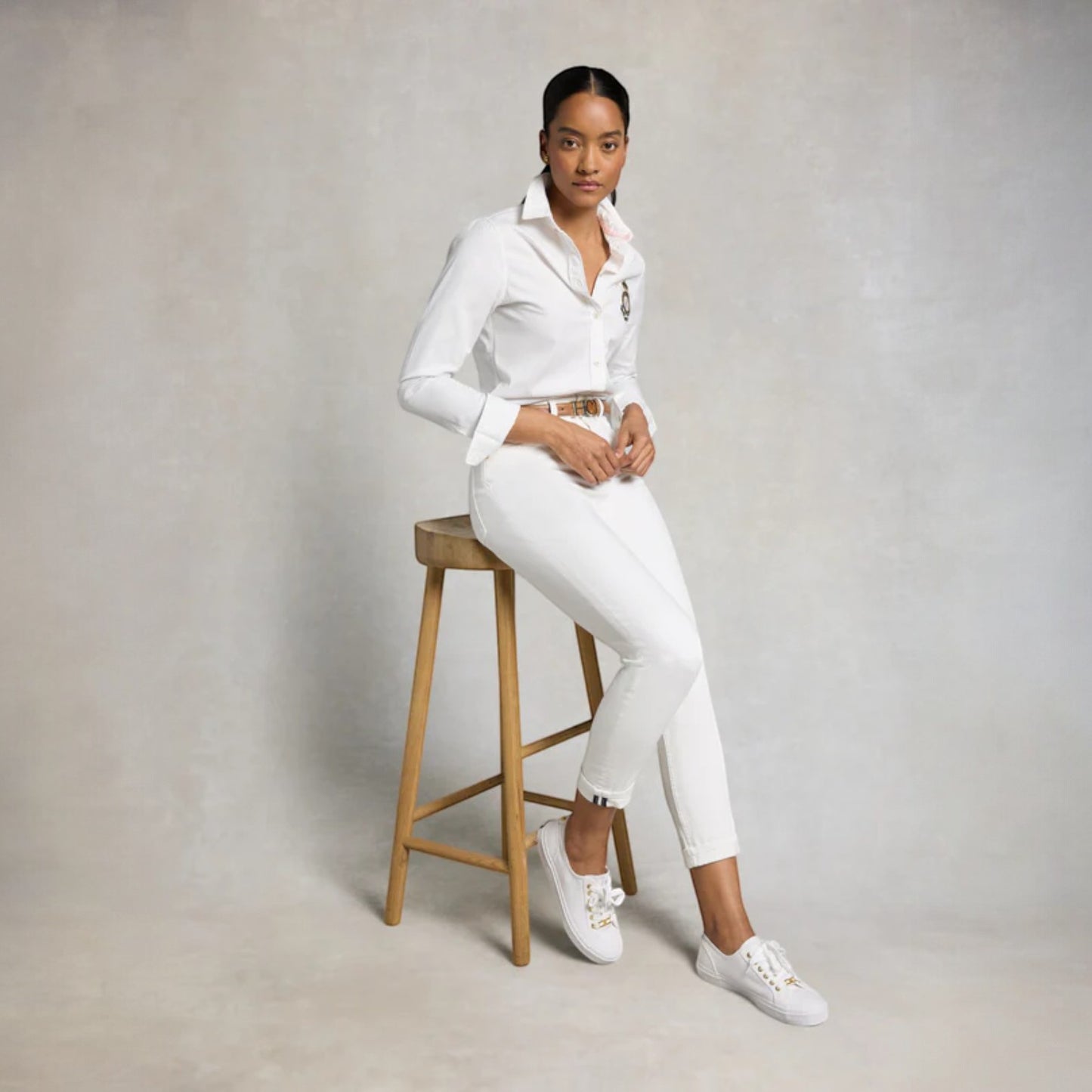 Person wearing a white outfit sitting on a wooden stool against a plain background