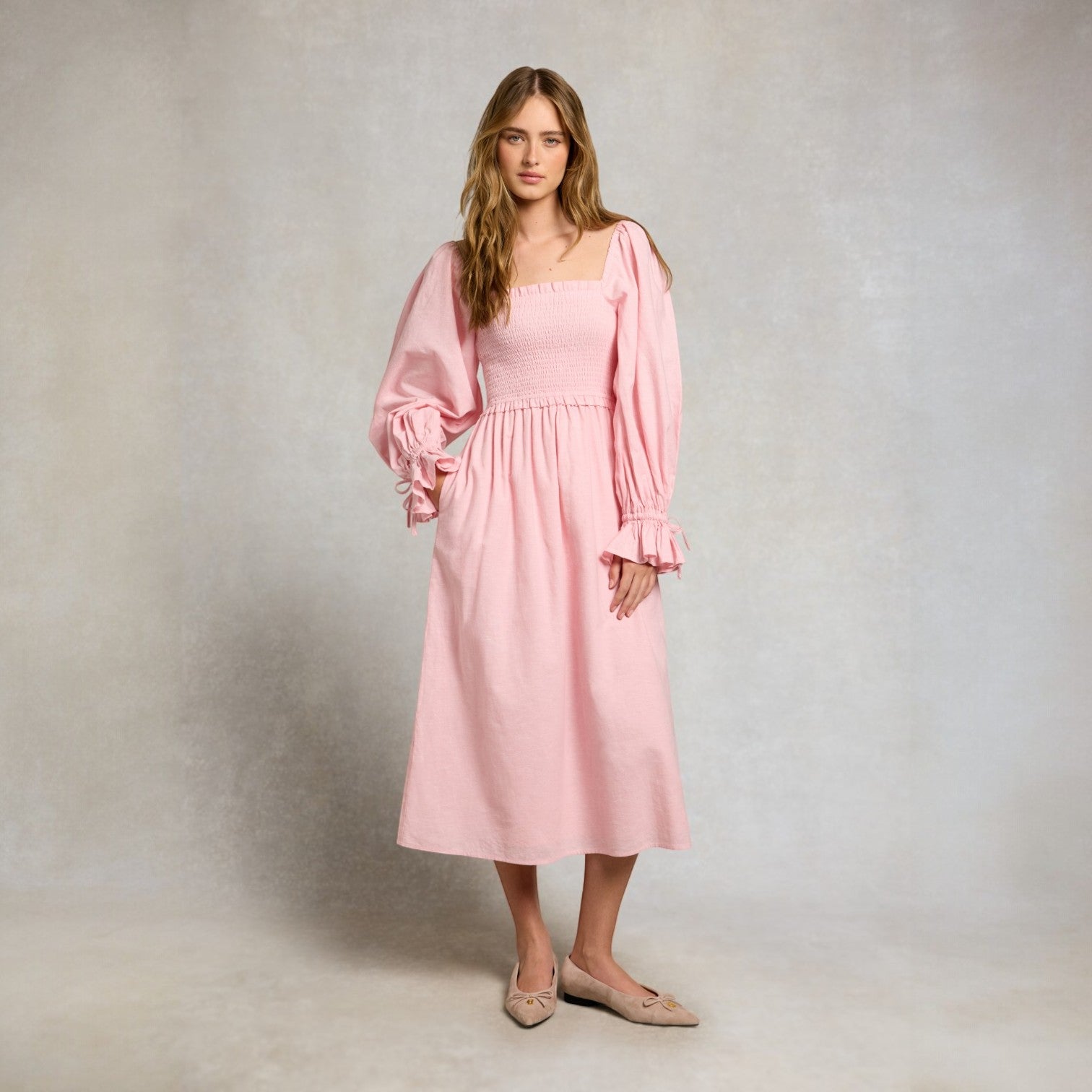 Woman wearing a pink dress with long sleeves against a plain background