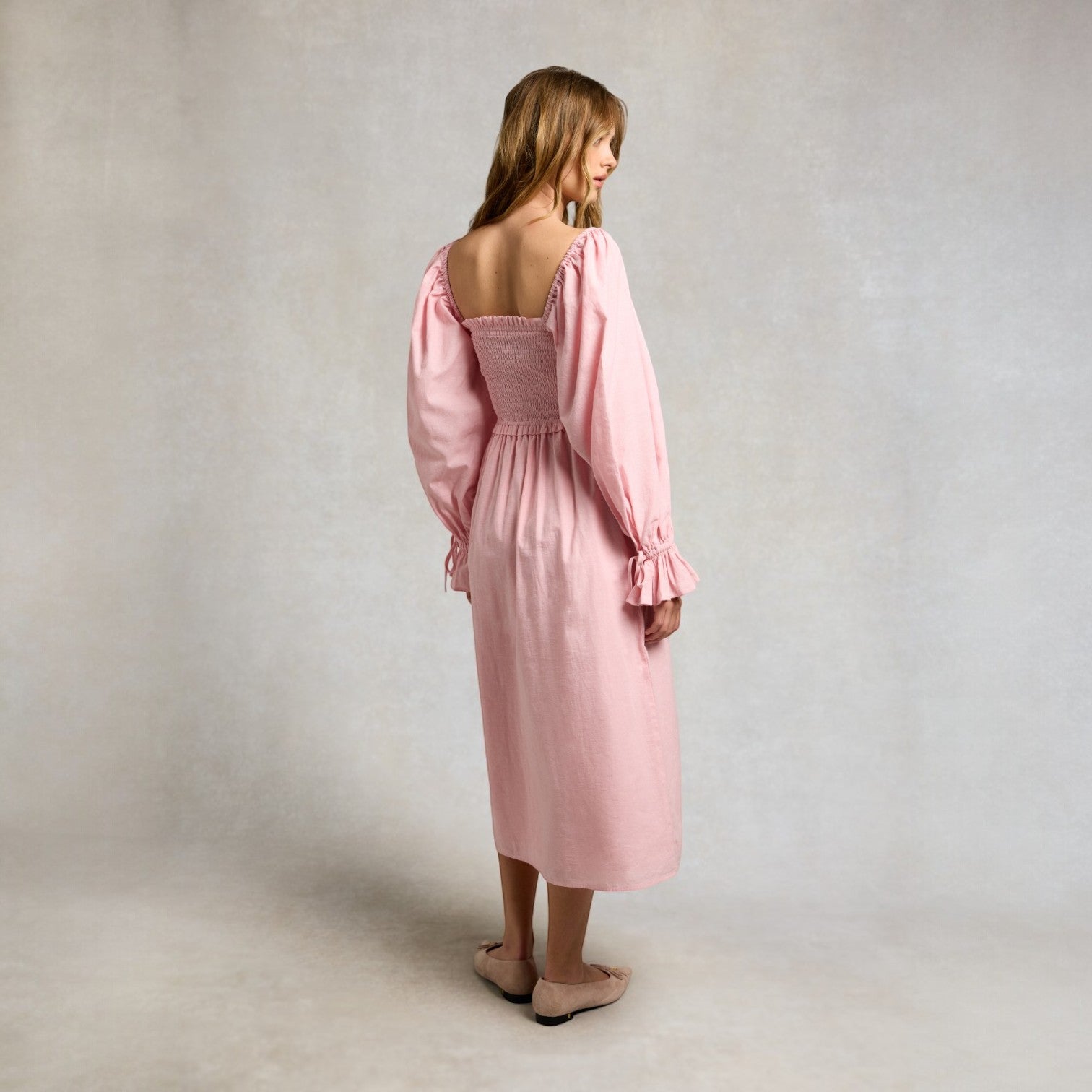 Woman wearing a pink dress with long sleeves against a plain background