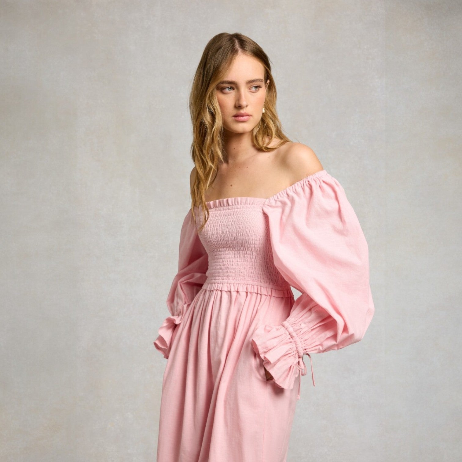 Woman wearing a pink off-shoulder dress against a plain background