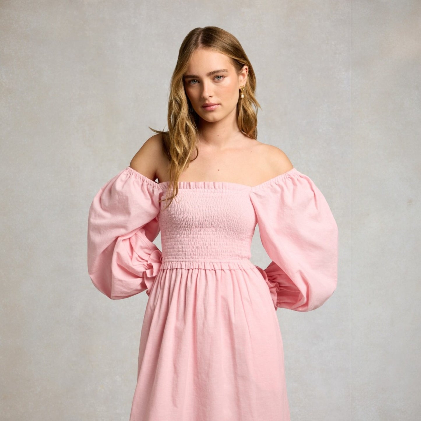 Woman wearing a pink off-shoulder dress with puffed sleeves against a plain background