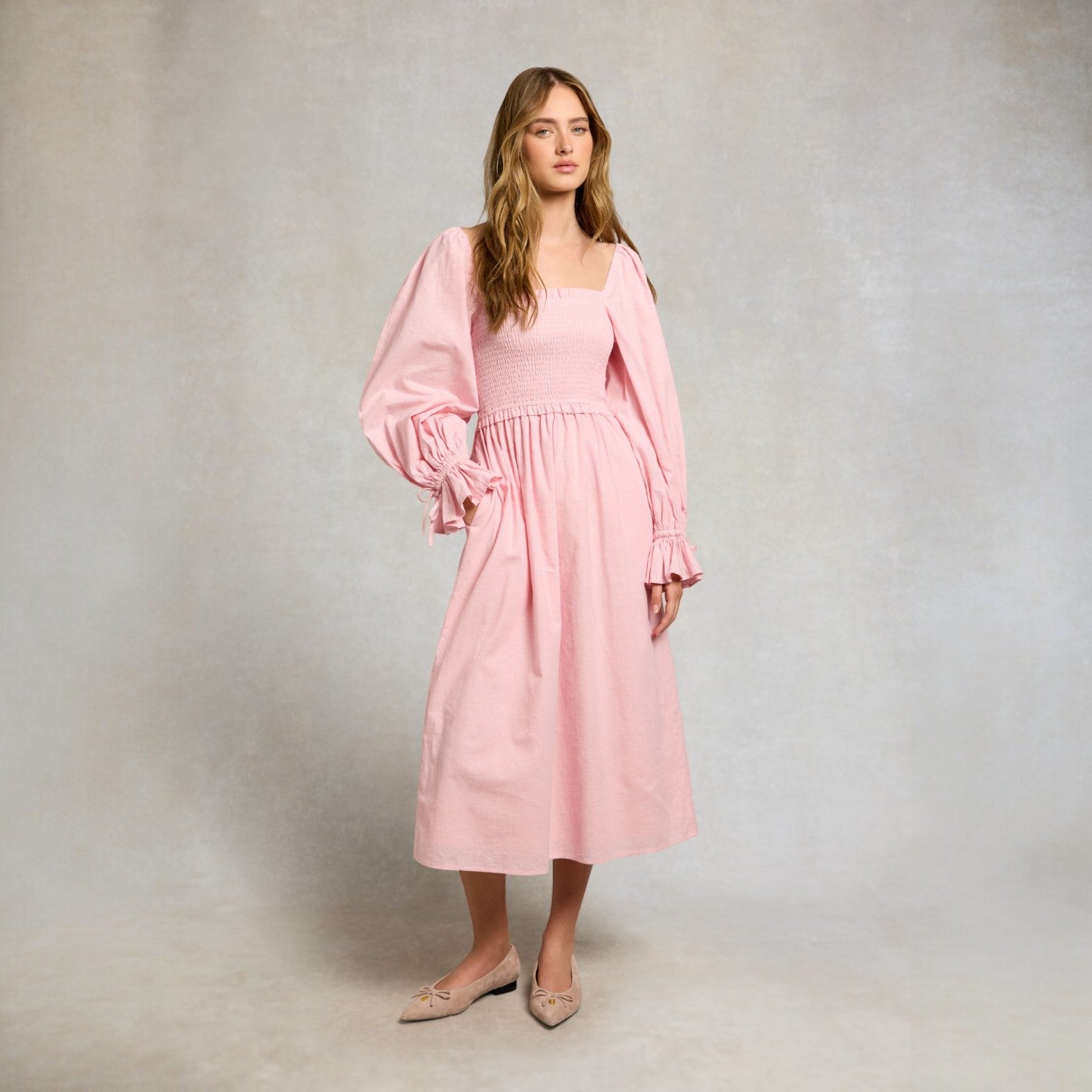 Woman wearing a pink dress with long sleeves against a plain background
