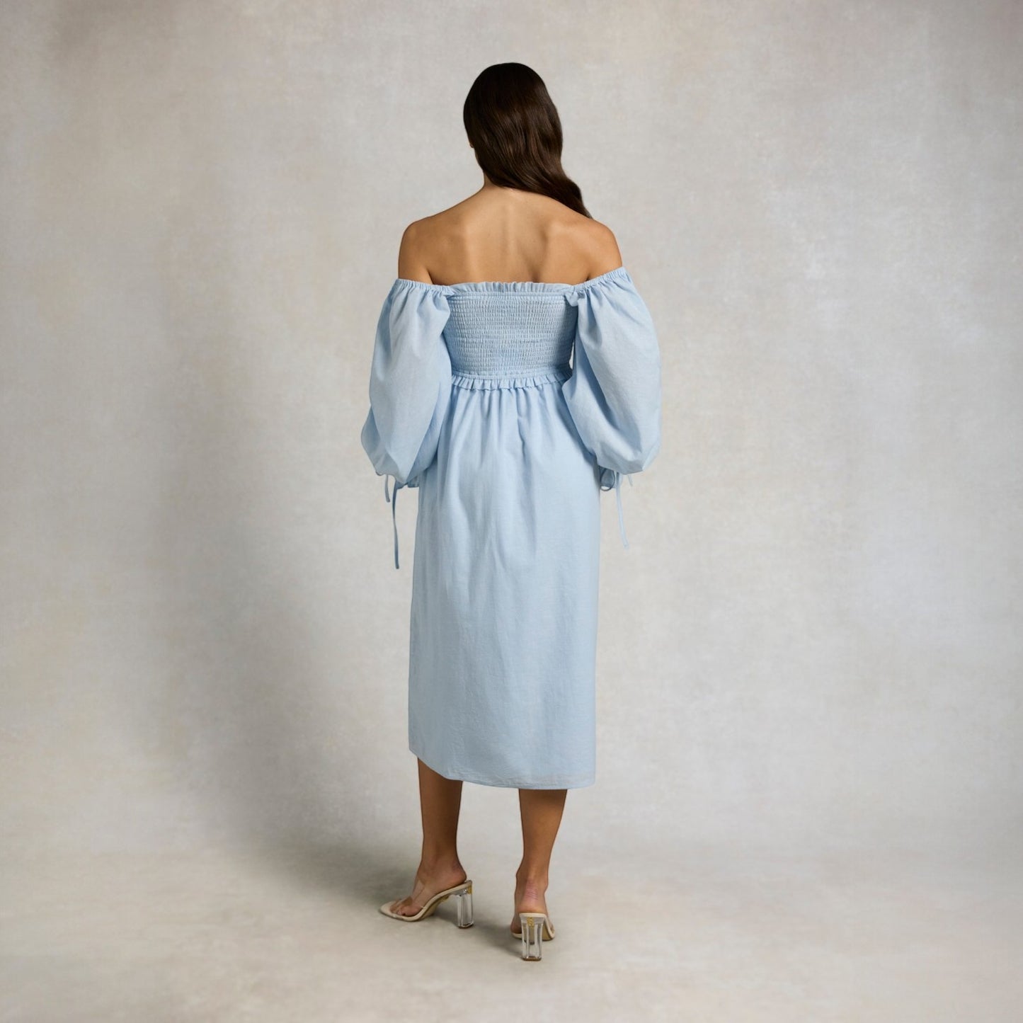 Woman wearing a light blue off-shoulder dress against a plain background