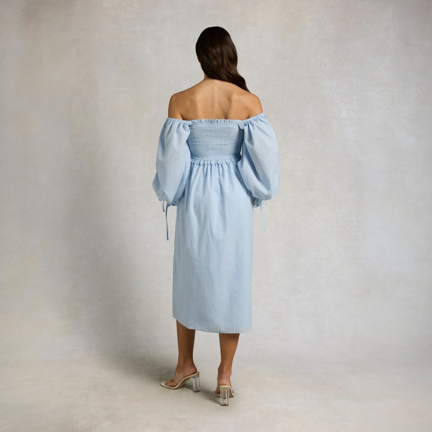 Woman wearing a light blue off-shoulder dress against a plain background