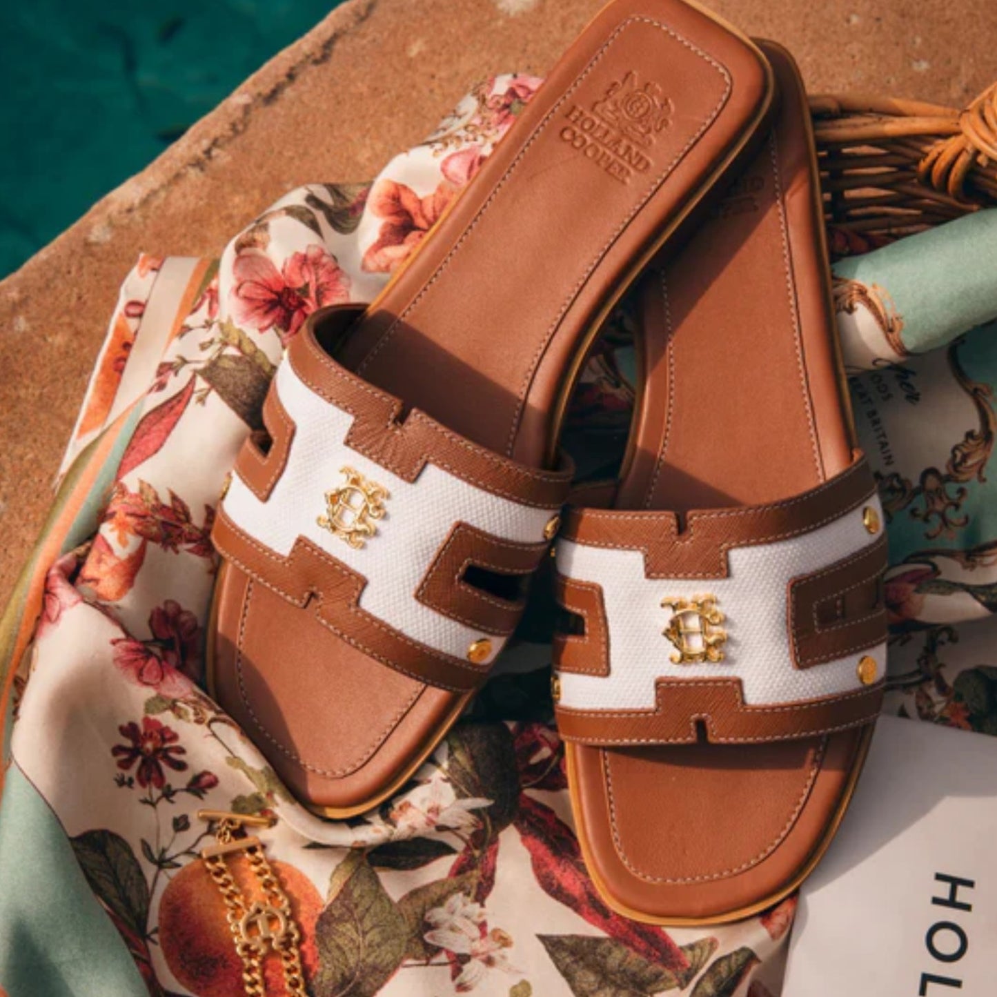 Brown and white sandals with a logo on a floral fabric background