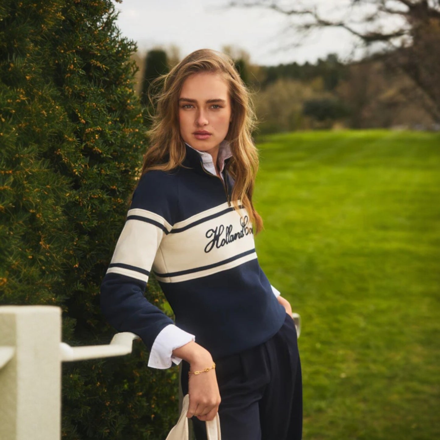 Woman wearing a navy and white striped sweater with 'Hollister' branding, standing outdoors.