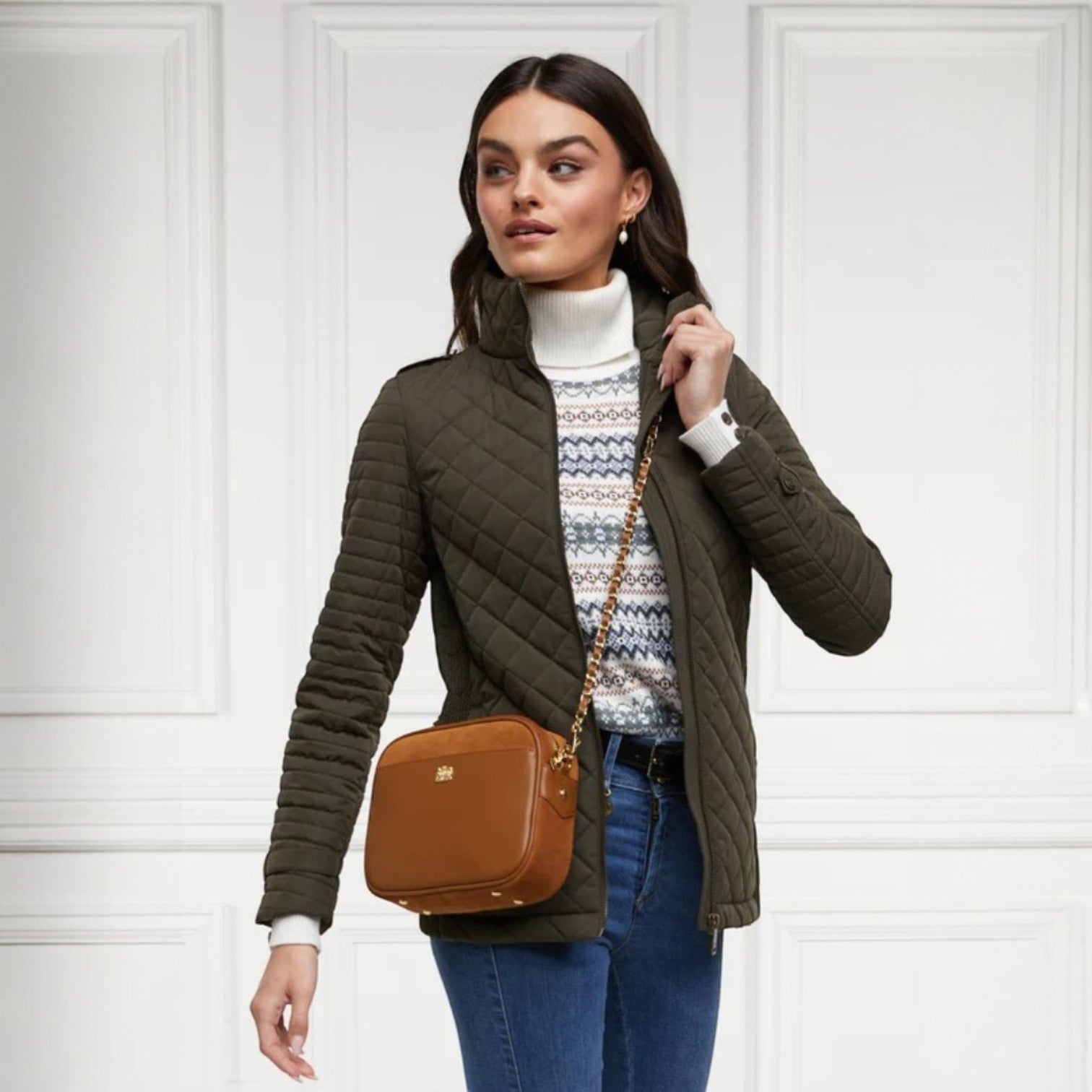 Woman wearing a green quilted jacket with a brown bag against a white paneled wall