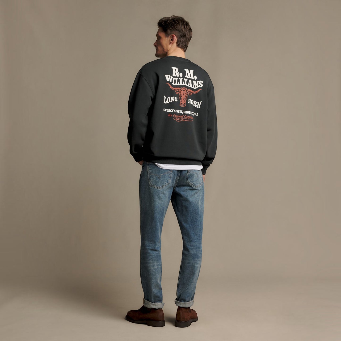 A man stands with his back to the camera wearing a black bomber jacket with a large white and red 'R.M.