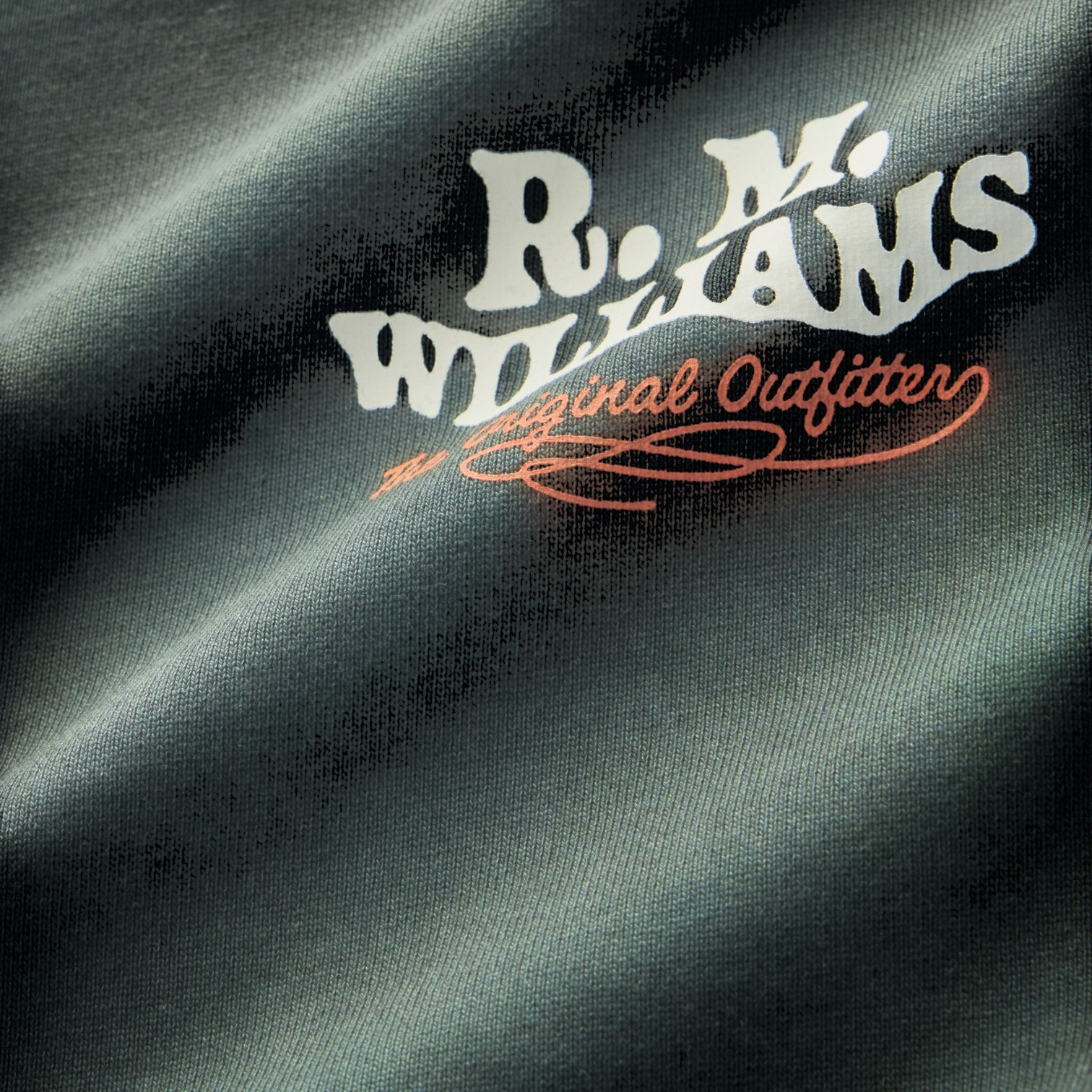 Close-up of a dark charcoal gray fabric with a printed logo reading 'R. M. Williams Original Outfitter' in white and orange.