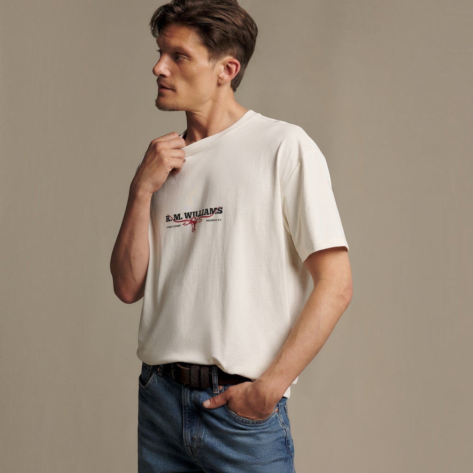 A man wearing a cream-colored short-sleeve t-shirt with a black and red 'R.M.