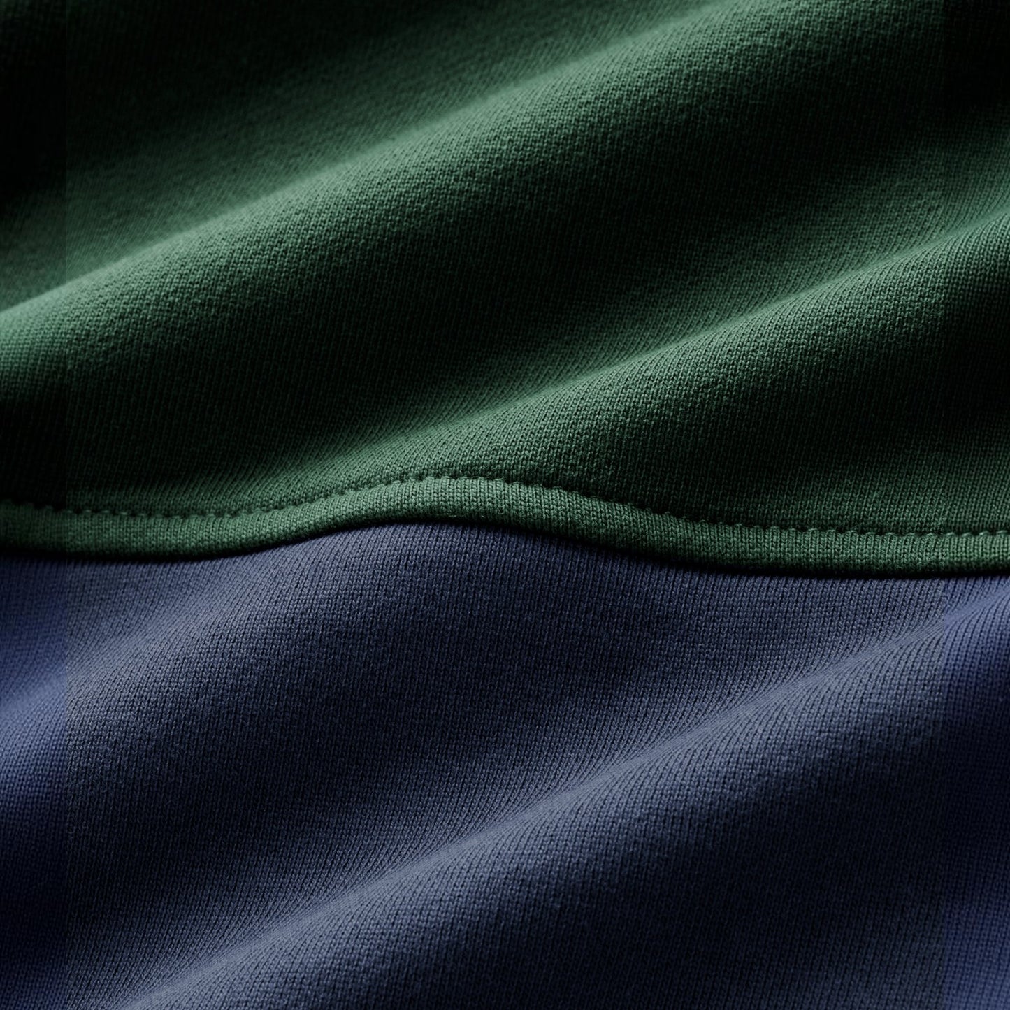 Close-up of a two-tone fabric product, showing a dark green upper section with a stitched seam and a dark navy lower section.